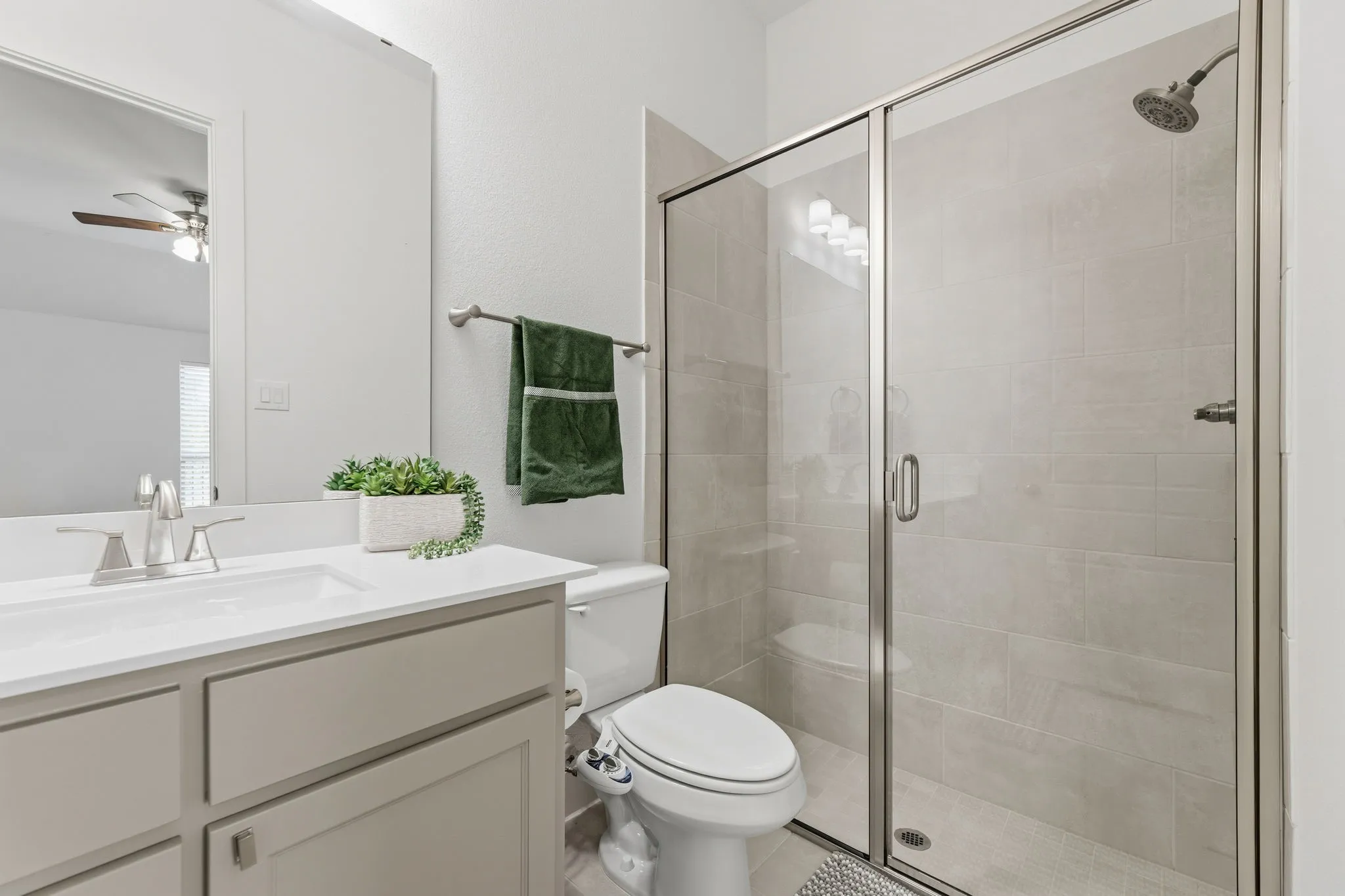 Bathroom featuring a glass-enclosed shower with tile surround, a single vanity with an integrated sink, polished chrome faucet, and a large wall-mounted mirror
