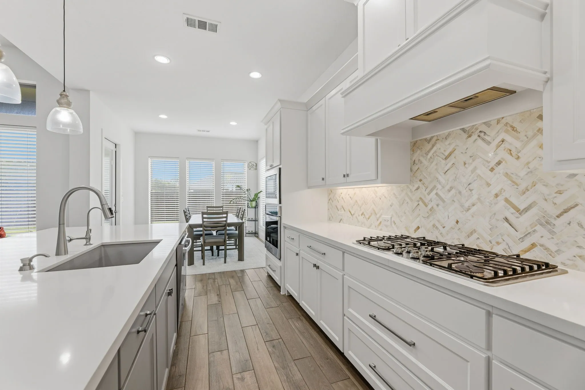 Modern kitchen featuring wood-finish flooring, white cabinetry, a gas cooktop, and a herringbone-patterned backsplash