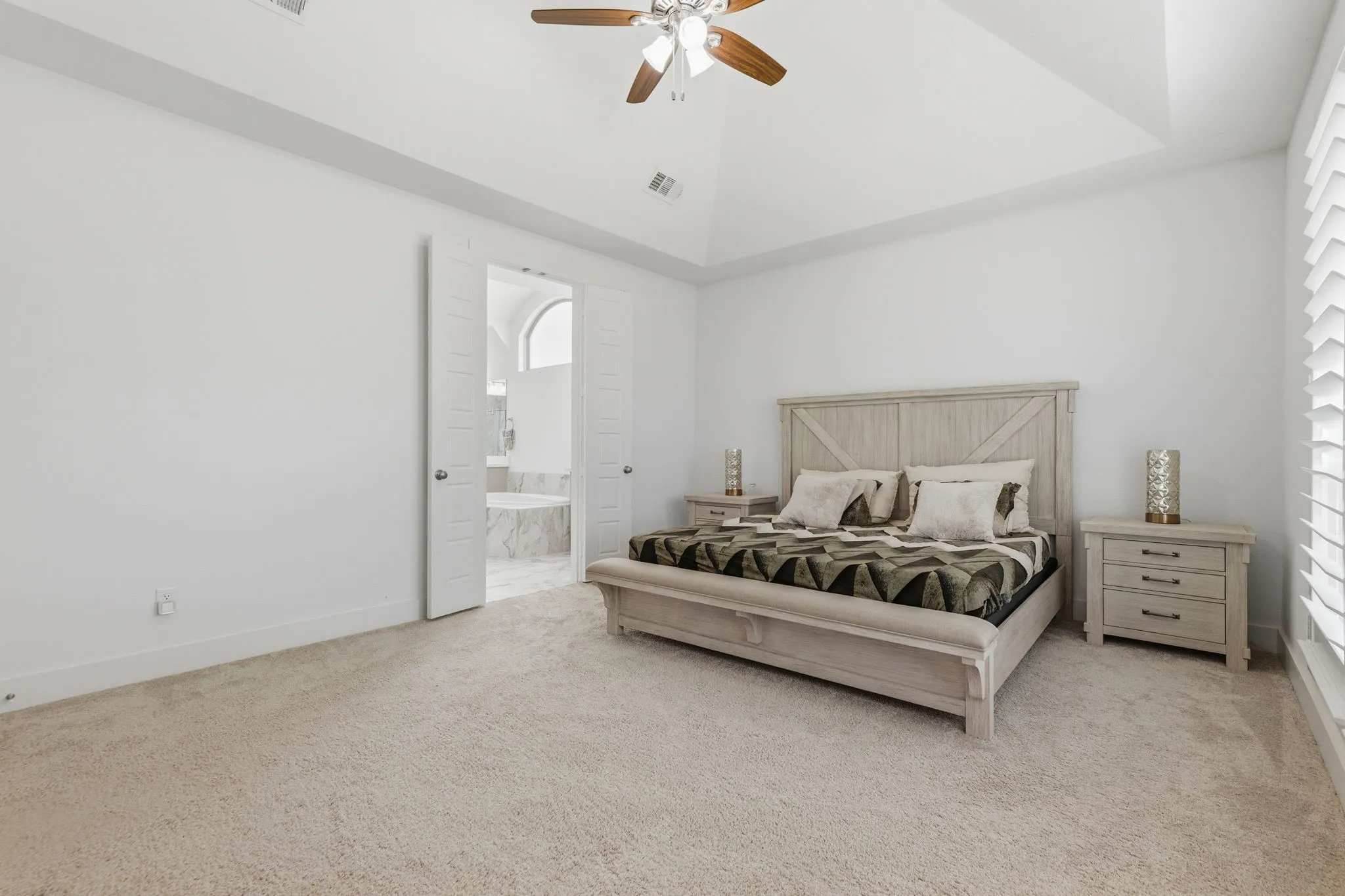 Spacious room featuring vaulted ceilings, a ceiling fan with integrated lighting, plush carpet flooring, and plantation shutters
