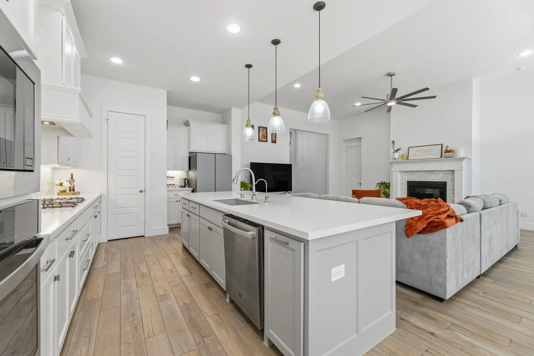Spacious kitchen featuring an extended island with a built-in sink and stainless steel dishwasher, white cabinetry, wood-finish flooring, and recessed lighting