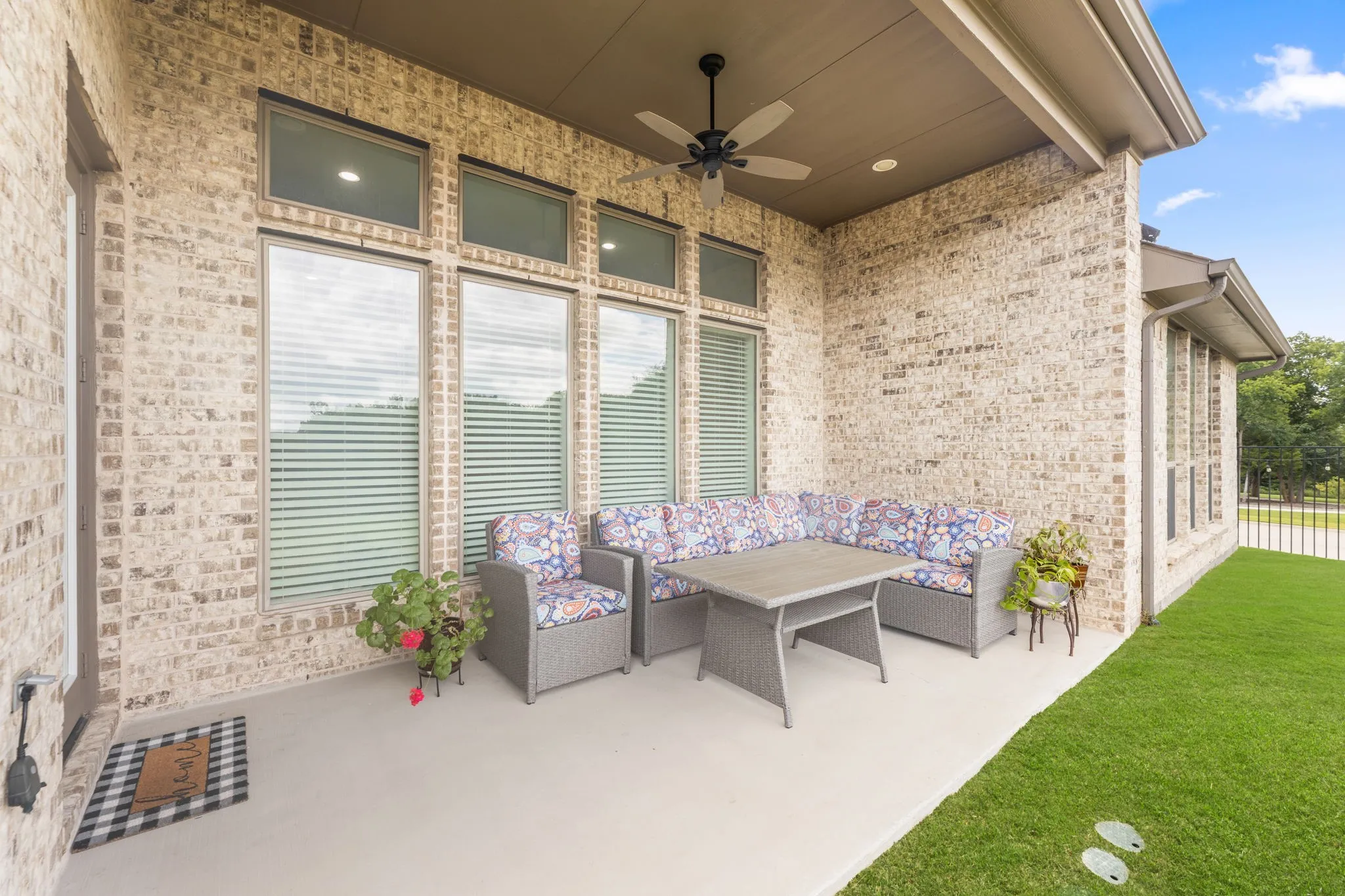 Covered patio featuring a ceiling fan, light-toned brick exterior, concrete flooring, and multiple windows with blinds