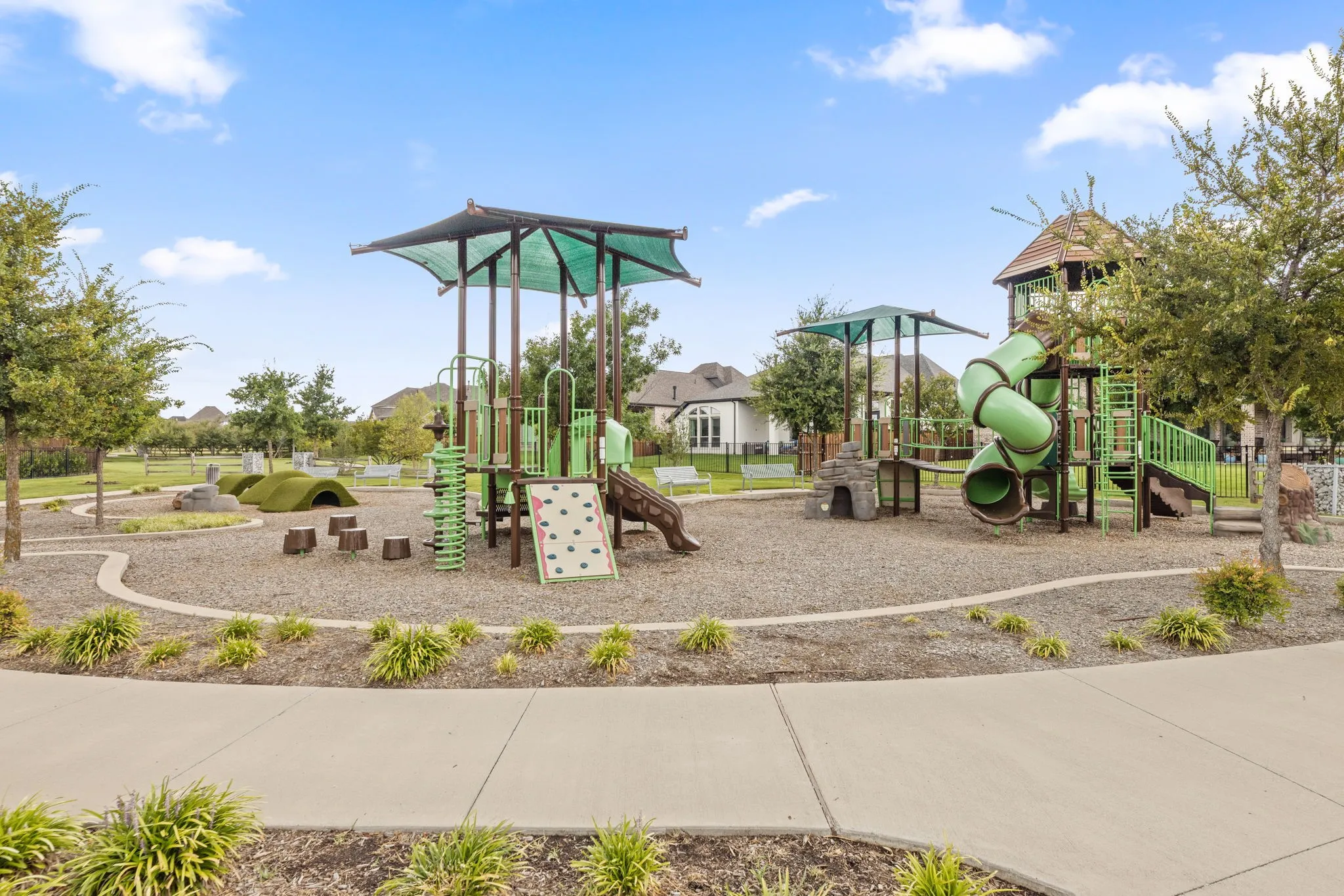 Community playground featuring multiple play structures, slides, climbing walls, and shaded areas