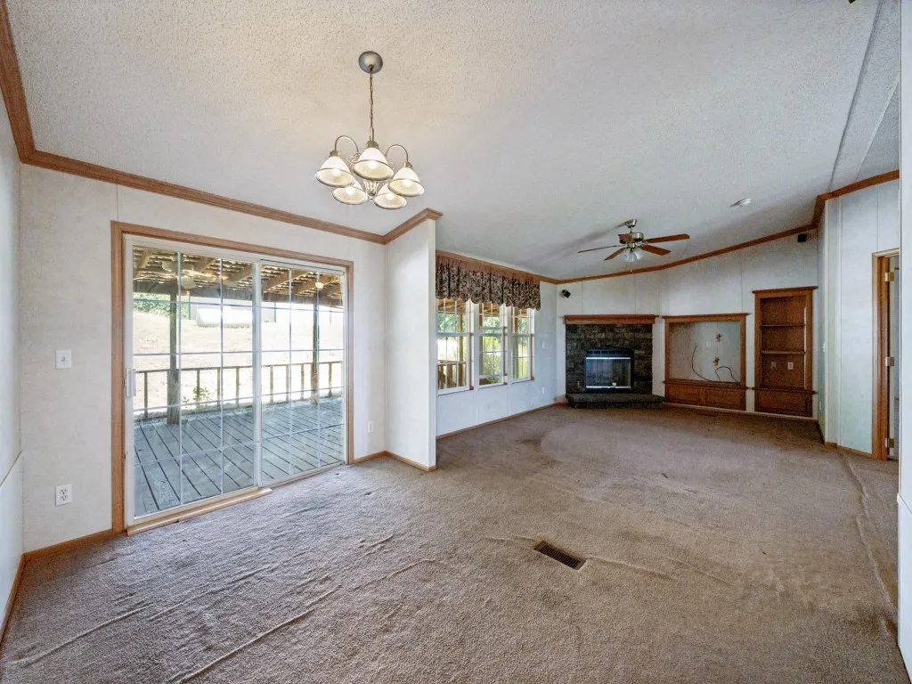 Spacious interior featuring a fireplace, built-in shelving, wood-trim walls, a ceiling fan, and sliding glass doors opening to an outdoor deck