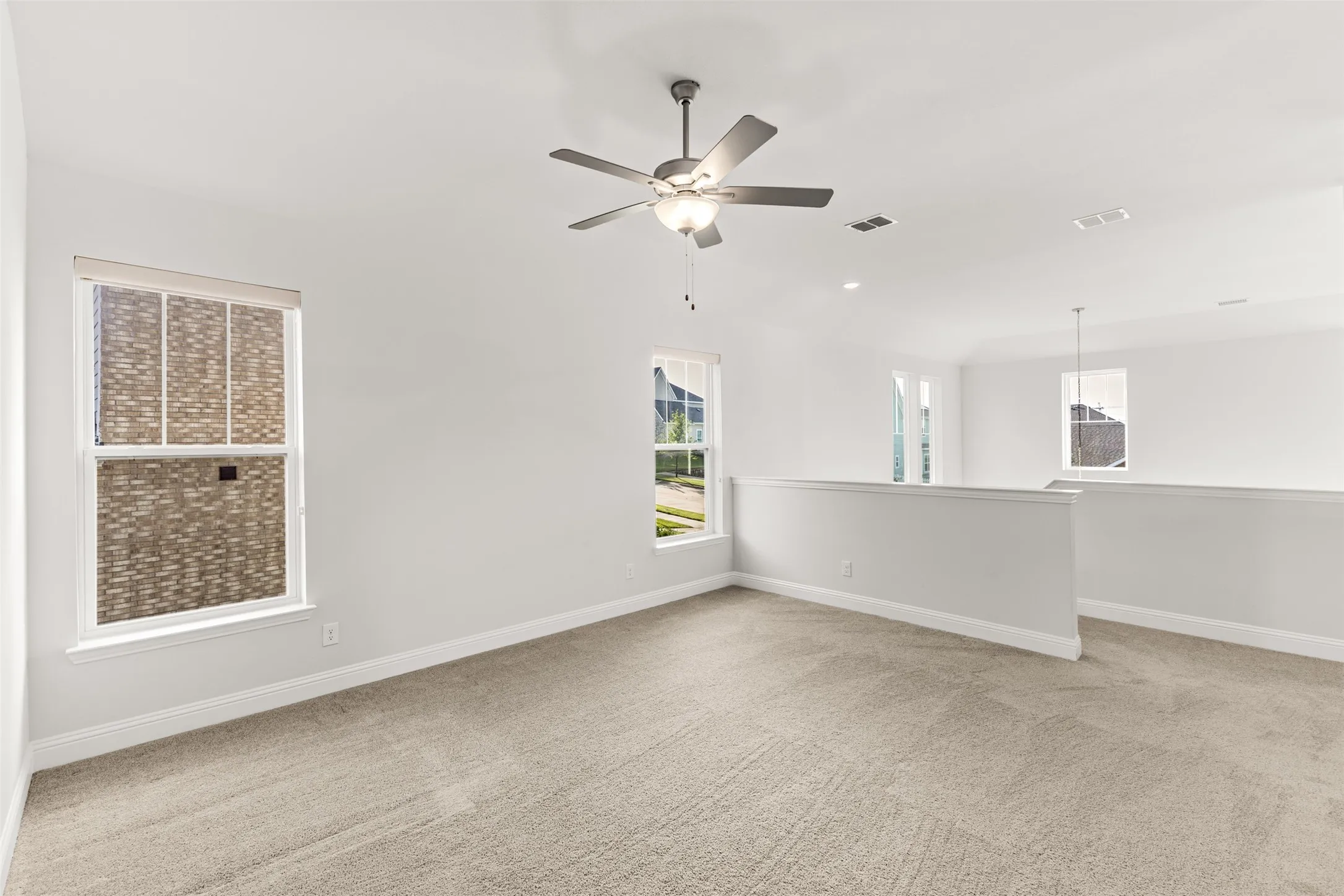 Spacious loft area featuring neutral carpeting, a ceiling fan with integrated lighting, and multiple windows