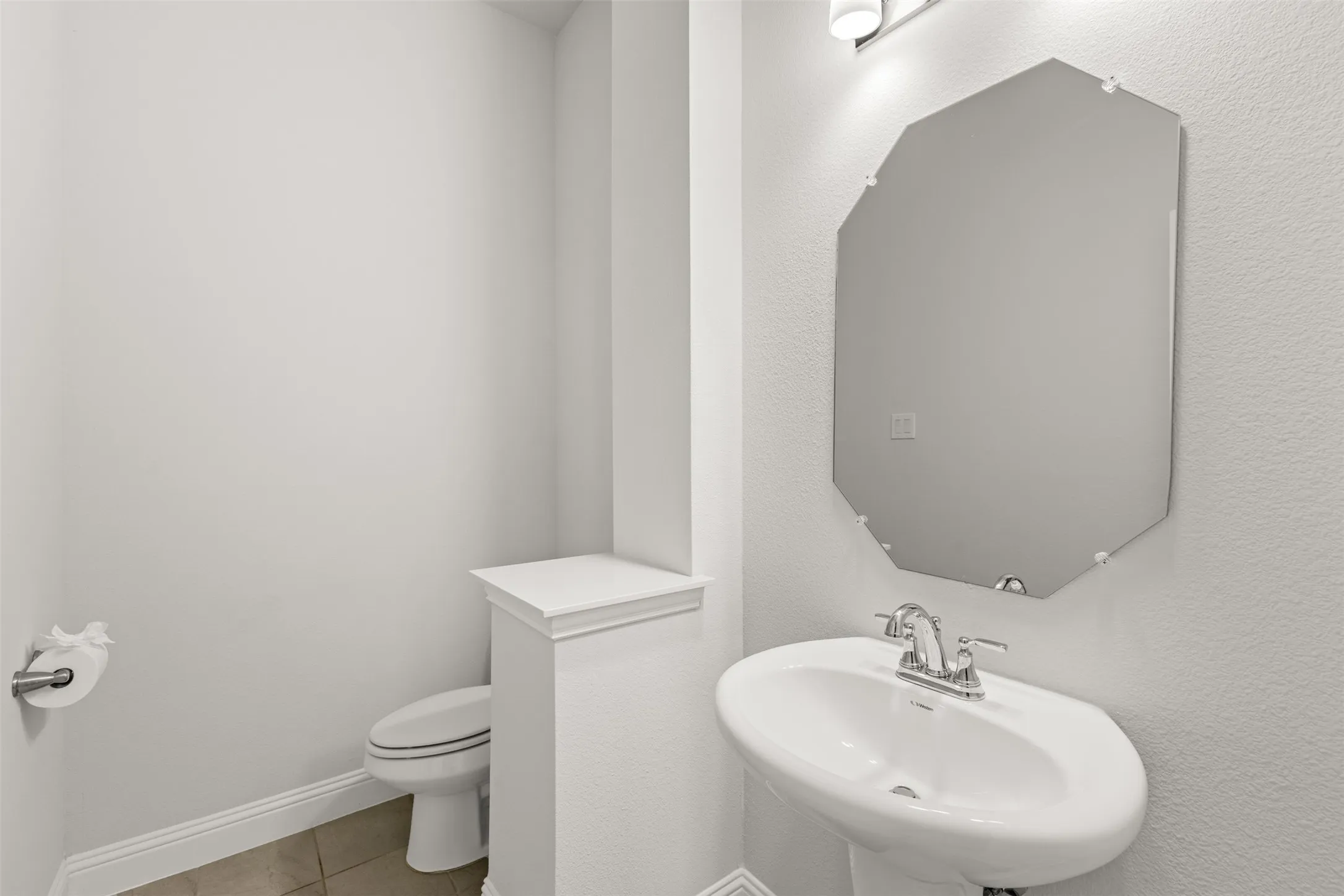 Powder room featuring a pedestal sink with chrome faucet, an octagonal mirror, and a commode