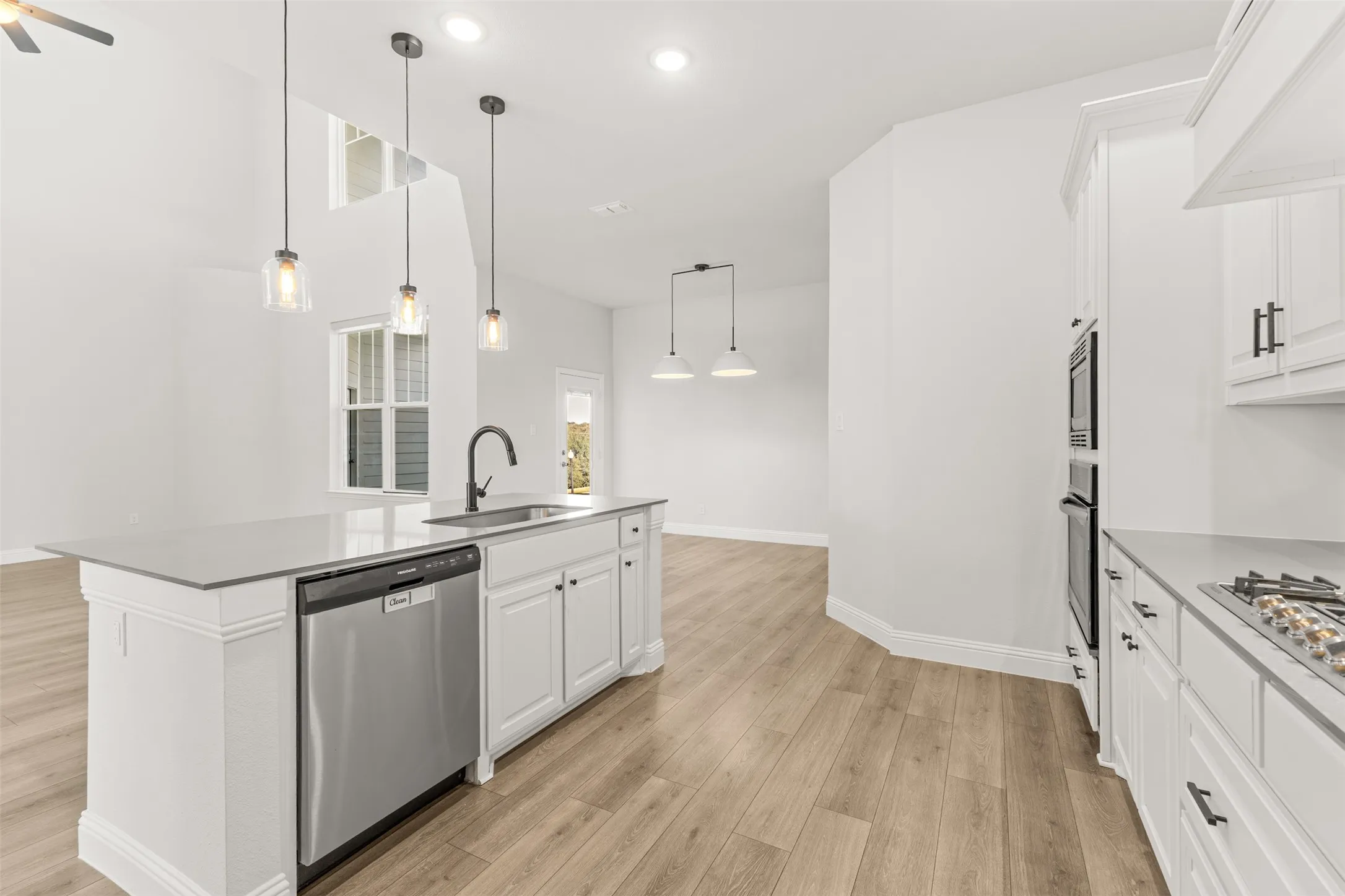 Open-concept kitchen featuring a spacious island with a sink, stainless steel dishwasher, light wood-finish flooring, white cabinetry with dark hardware, and recessed lighting