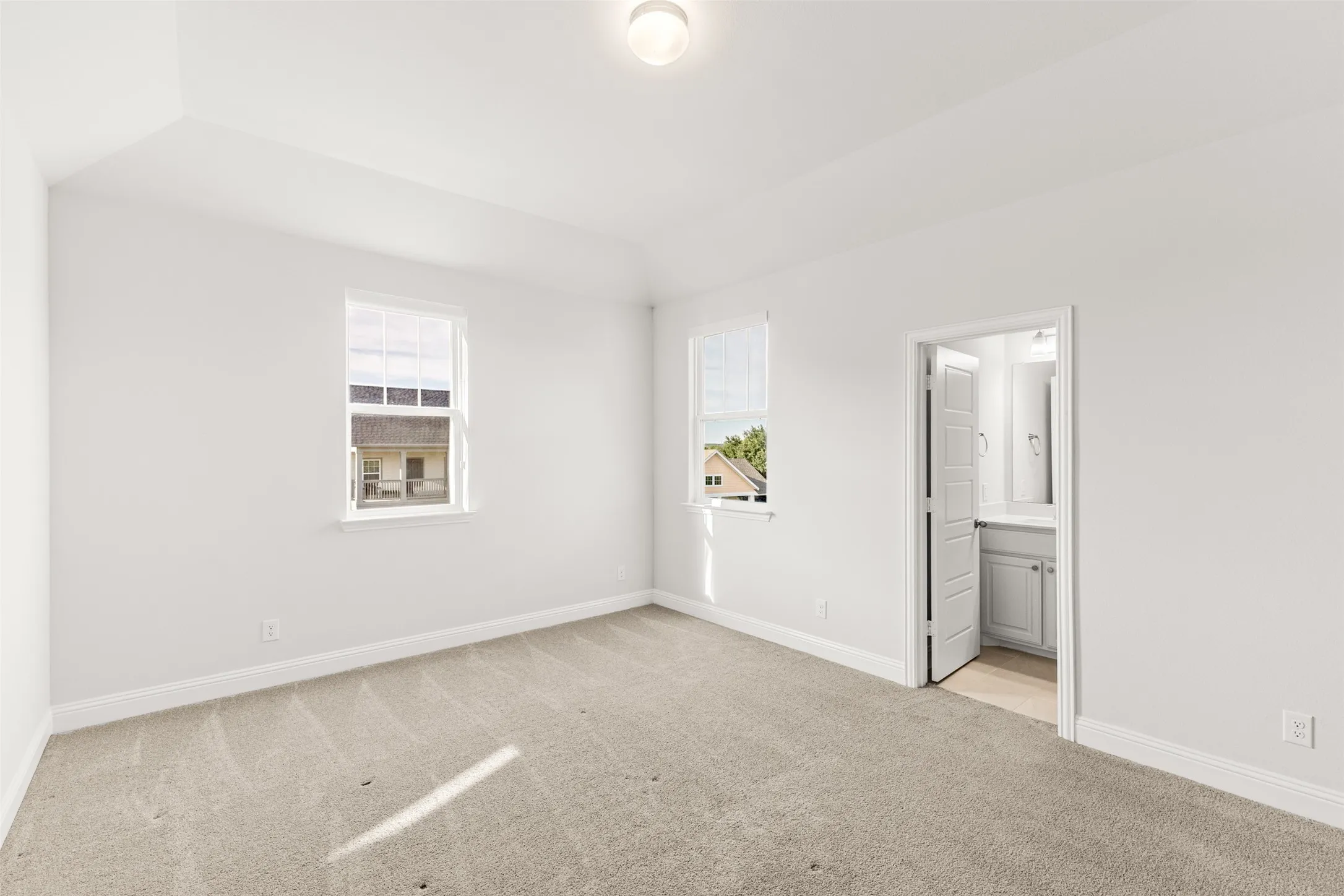 Spacious bedroom featuring light-colored carpeting, two windows, and an en-suite bathroom with a vanity and mirror