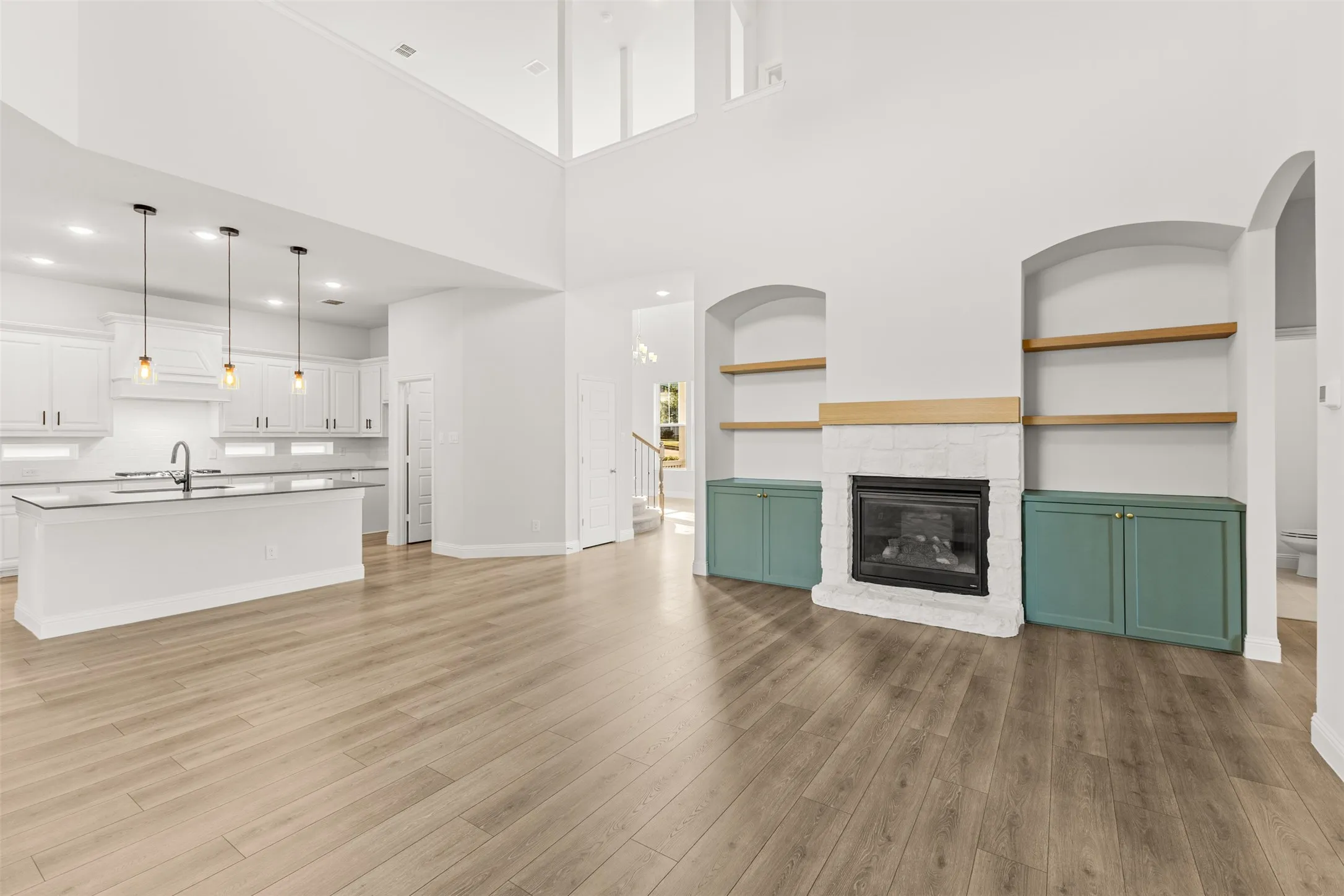 Open-concept living area featuring wood-finish flooring, a white-tiled fireplace with a wood mantle, and arched built-in shelving with teal base cabinetry