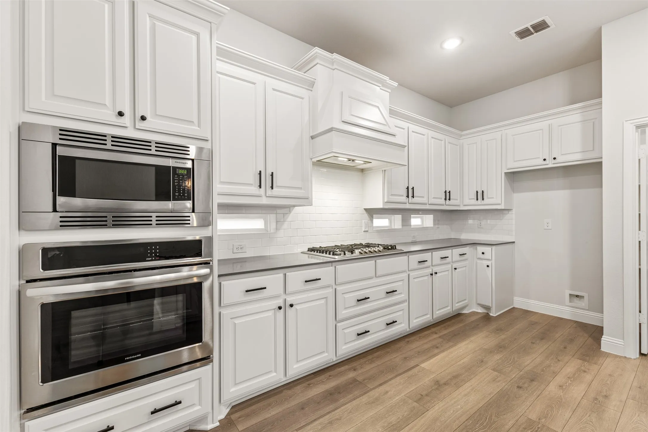 Modern kitchen featuring white cabinetry, stainless steel appliances, a gas cooktop, subway tile backsplash, and wood-finish flooring