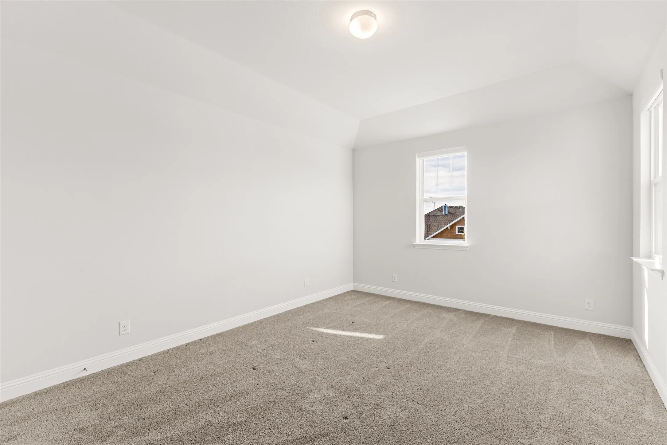 Bright room featuring vaulted ceilings, light gray carpeting, and a flush-mount ceiling light