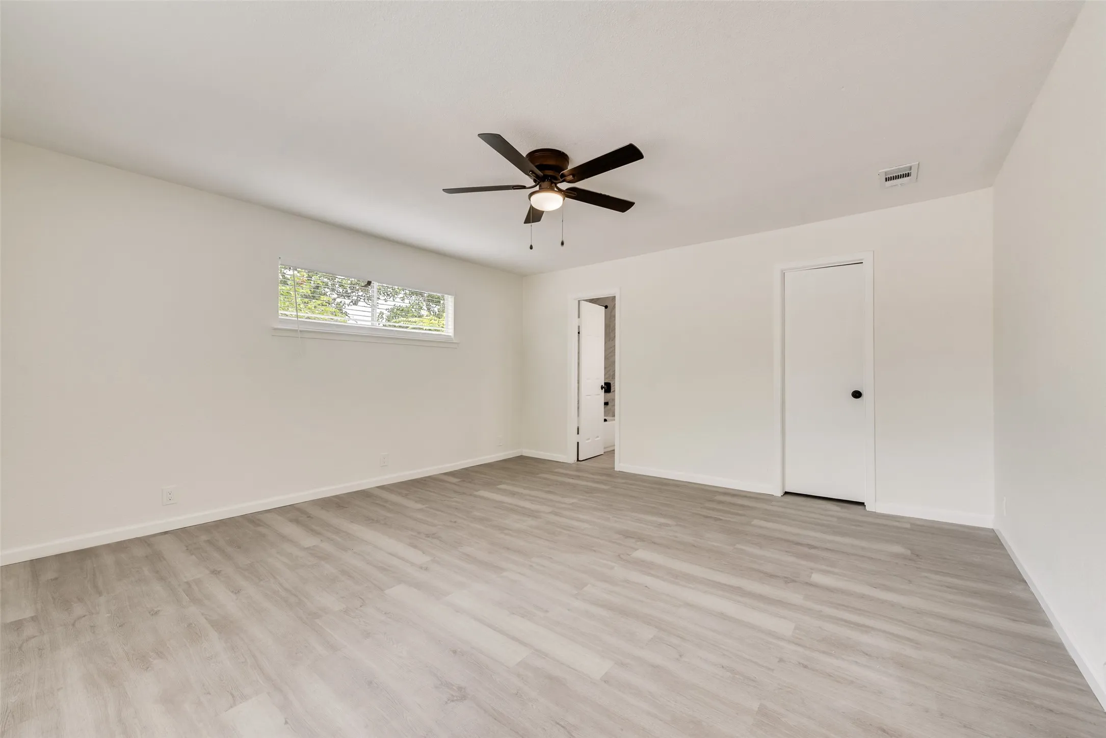 Spacious interior room featuring light-toned wood-finish flooring and crisp white walls