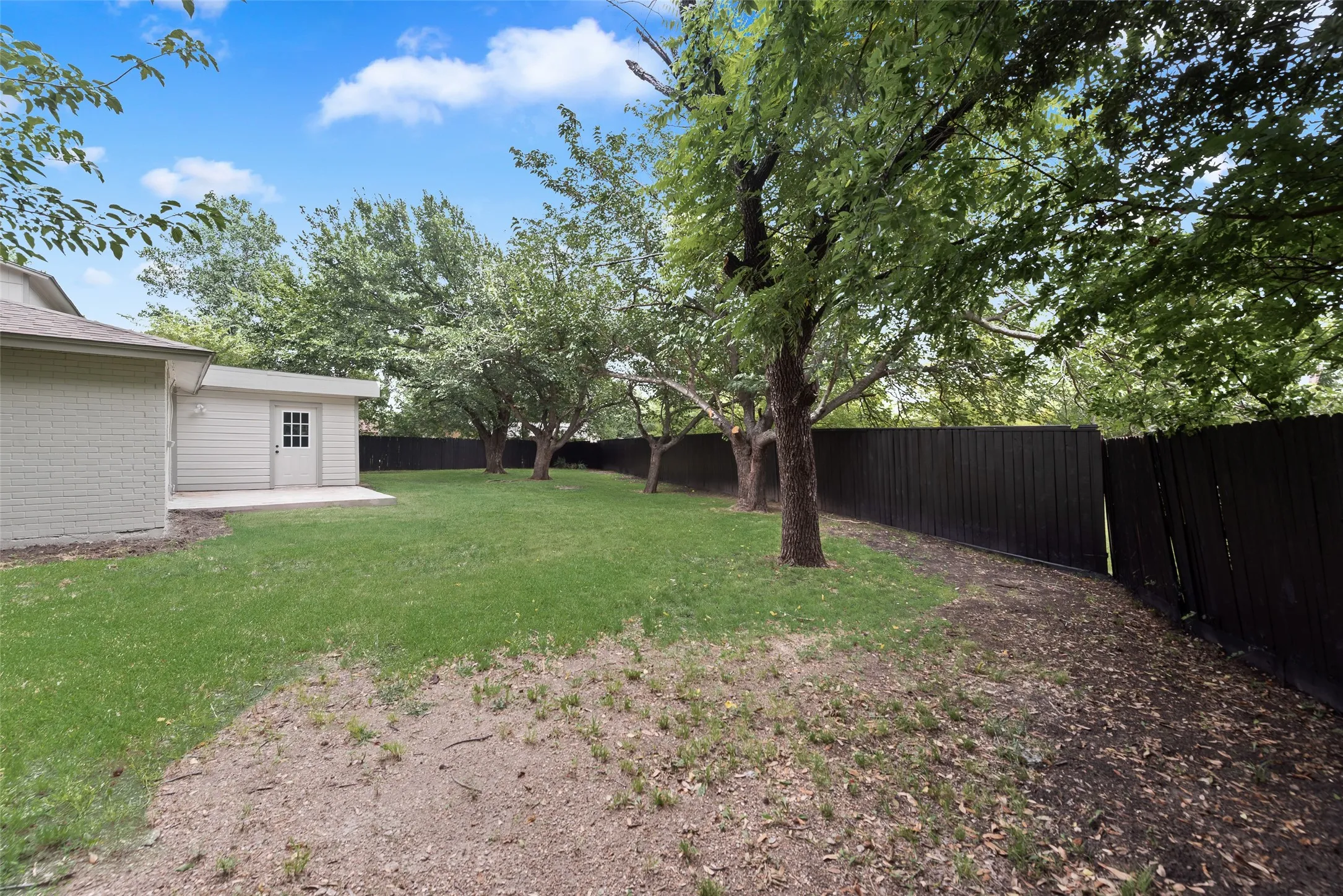 Expansive backyard featuring a manicured lawn, several mature trees, and a dark-stained wood privacy fence