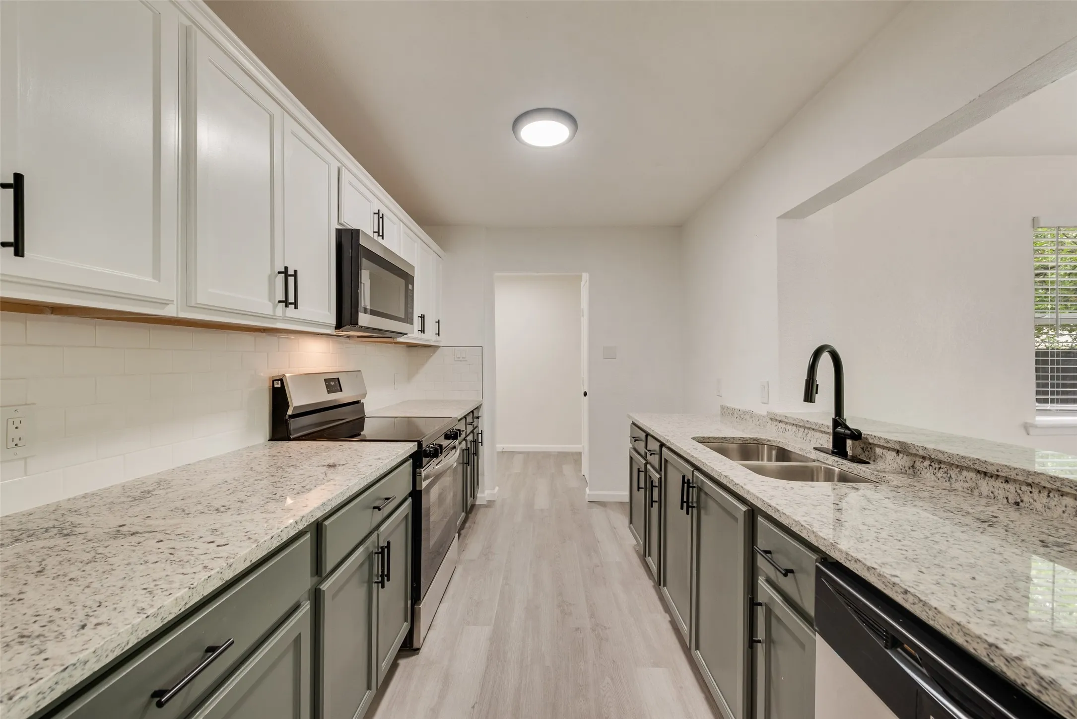 Galley kitchen with two-tone cabinetry, light-toned granite countertops, and wood-finish flooring