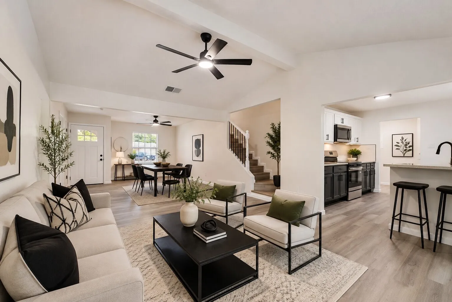 "Virtually Staged" Vaulted ceiling with exposed beams, wood-finish flooring, staircase with wood railing, kitchen featuring dark lower cabinetry and white upper cabinetry, and a peninsula with countertop seating