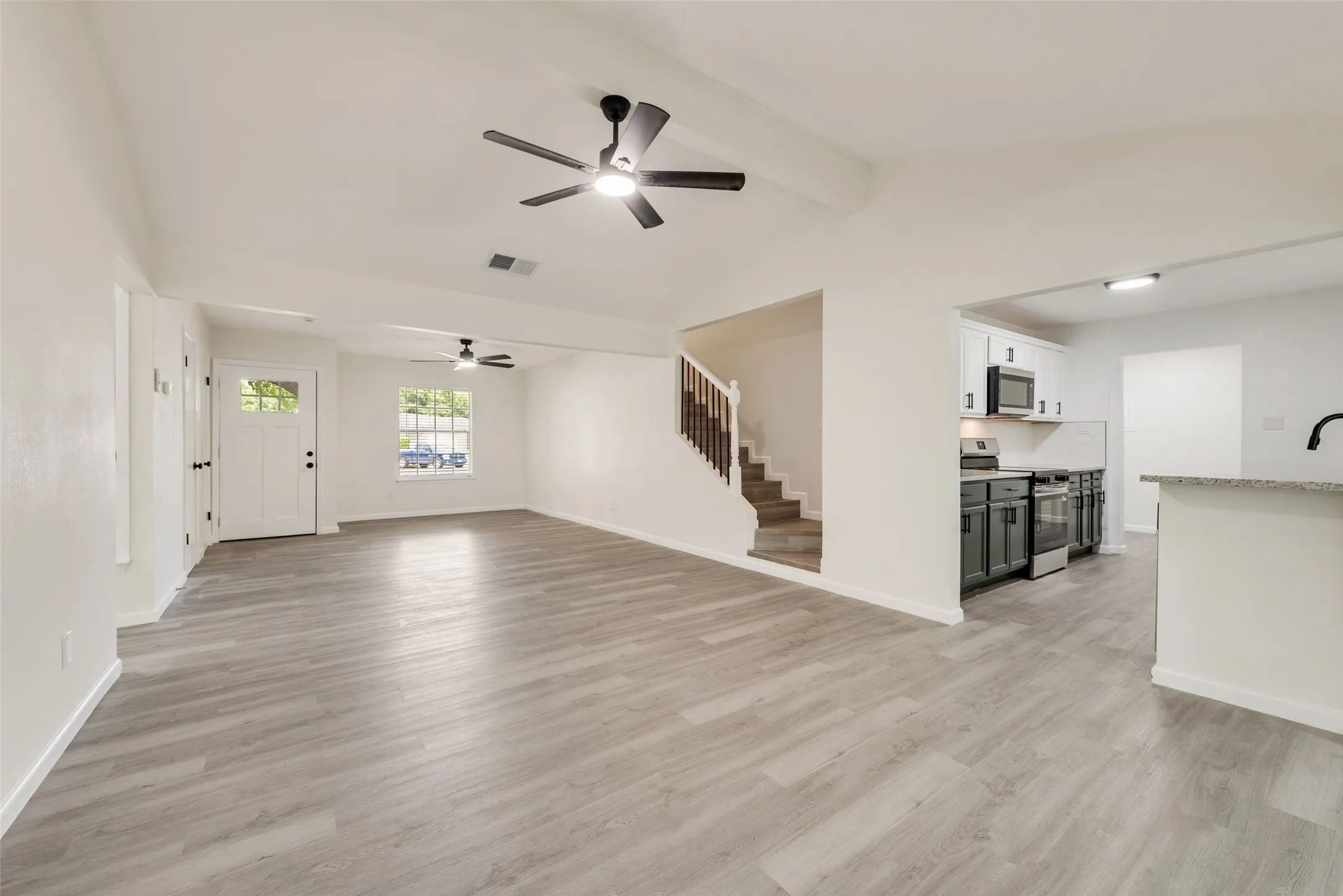 Expansive open-concept living area featuring light wood-finish flooring, a white paneled entry door with frosted glass, and multiple ceiling fans