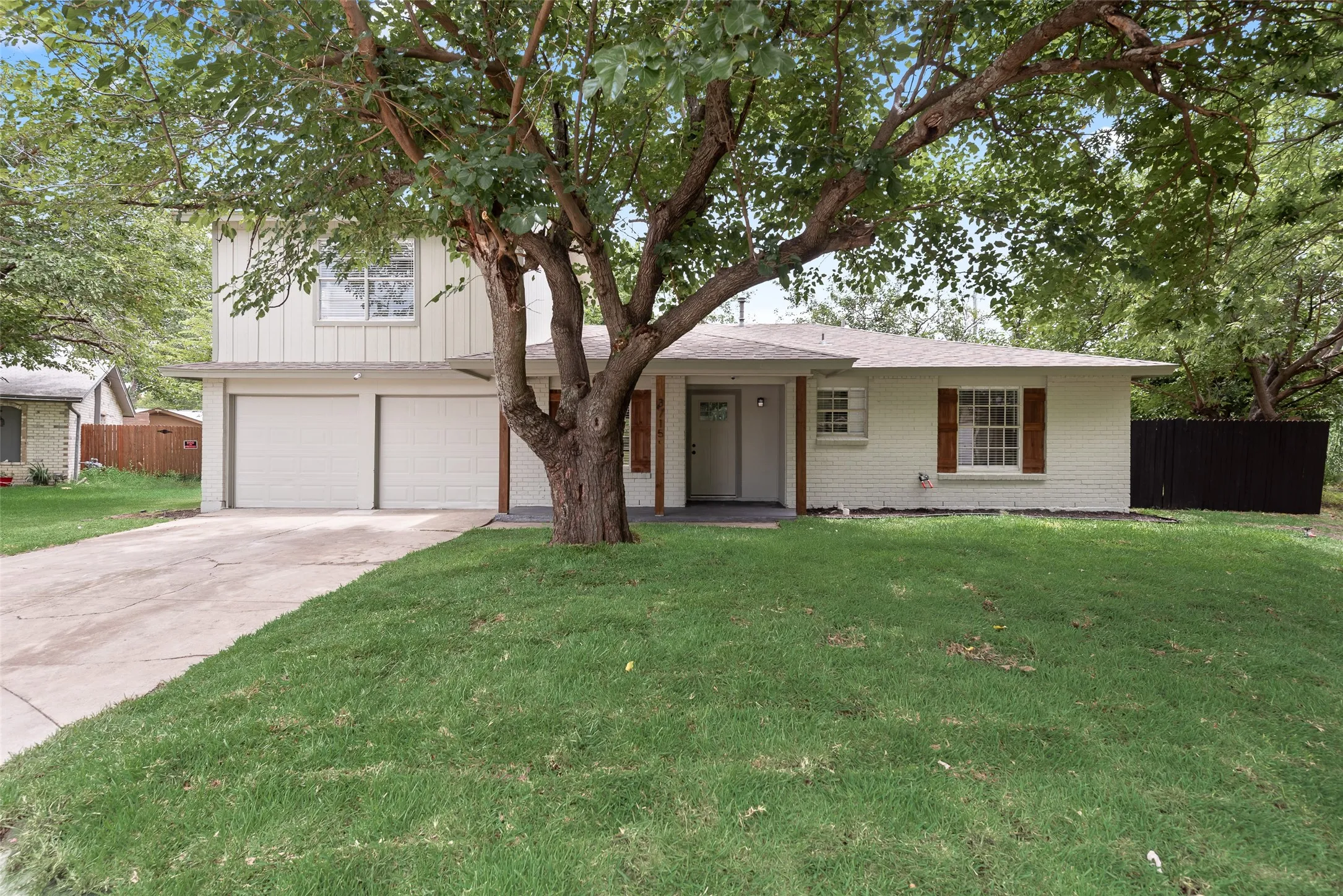 Split-level residence featuring a two-car garage, mature front yard tree, and an inviting entryway