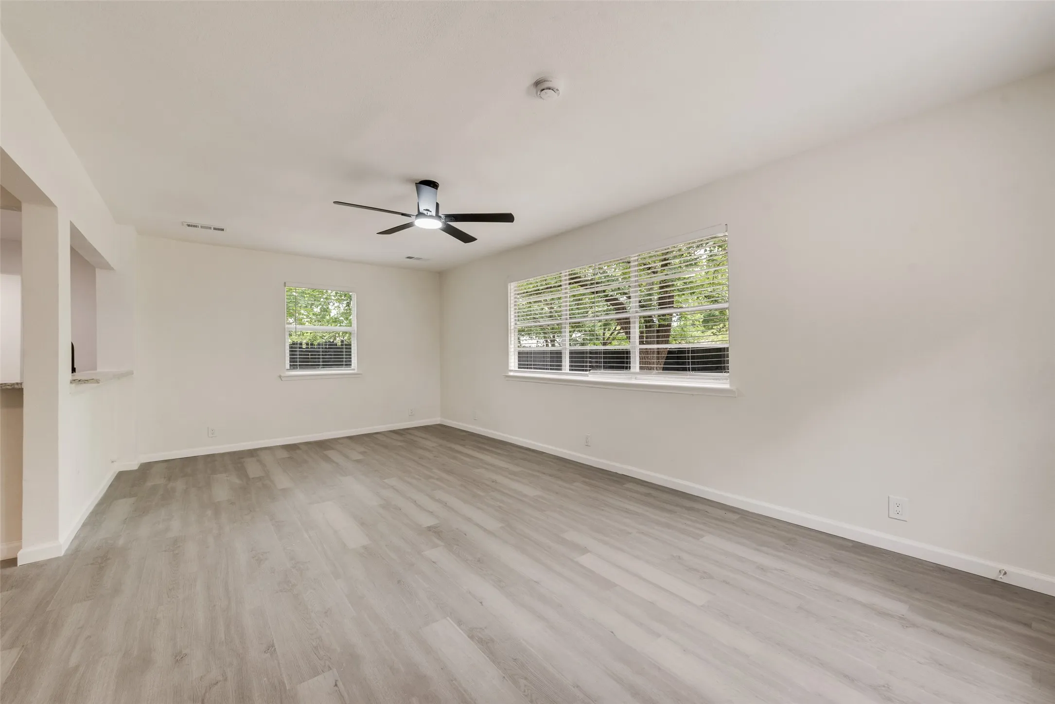 Spacious interior with wood-finish flooring, white walls, and a contemporary ceiling fan