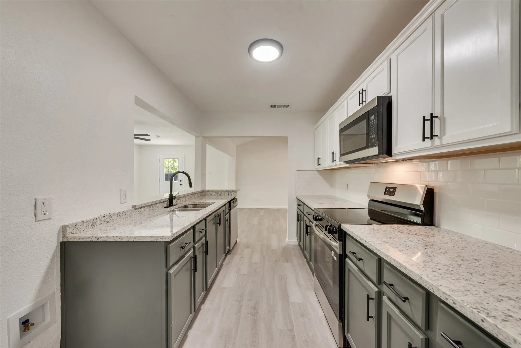 Modern kitchen featuring light-toned wood-finish flooring, two-tone cabinetry with white upper and dark lower cabinets, light-colored speckled countertops, and a white subway tile backsplash