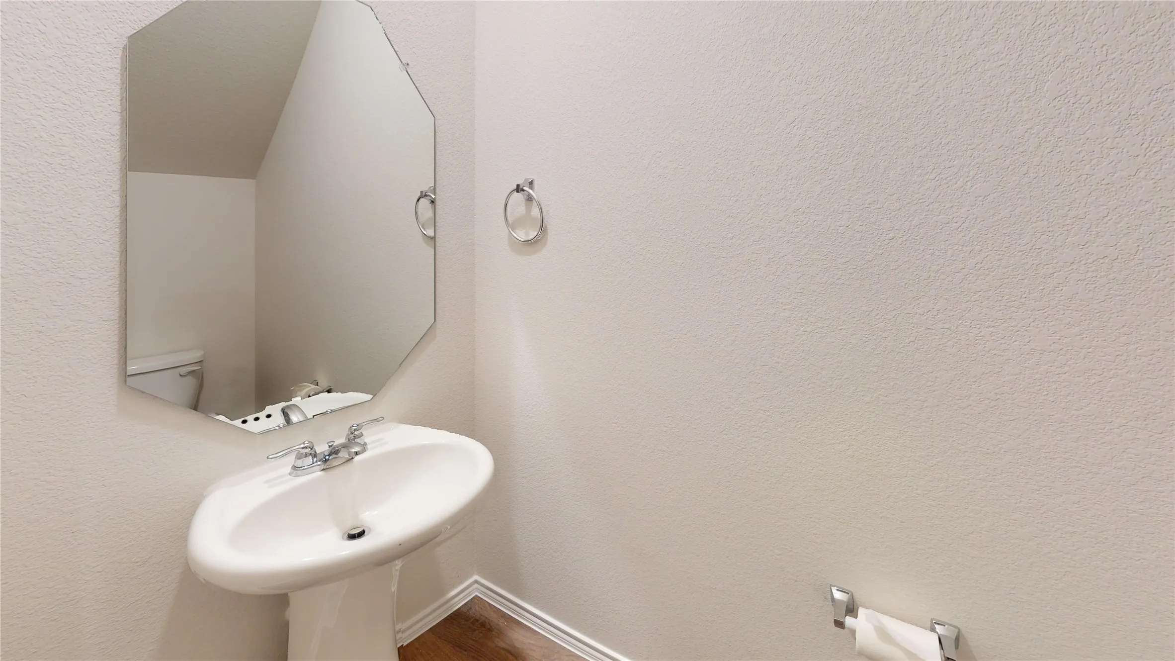 Pedestal sink with chrome faucet, complemented by a frameless octagonal mirror