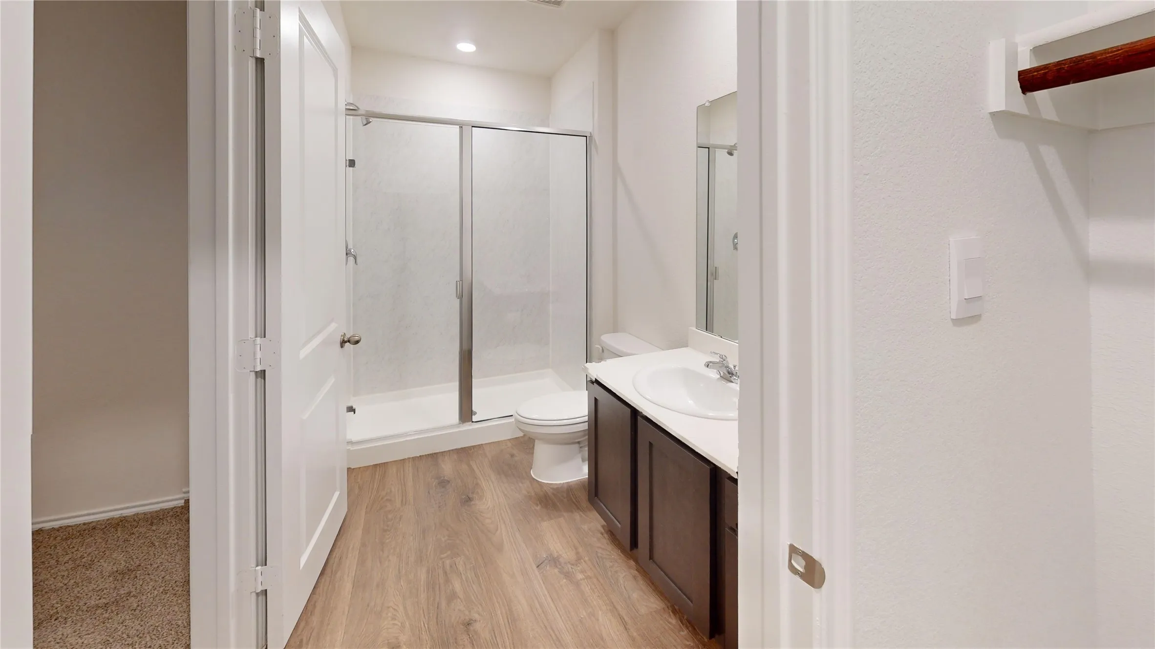 Bathroom featuring a glass-enclosed shower with a white pan, wood-finish flooring, a single vanity with a white countertop and integrated sink, and a dark wood-finish cabinet