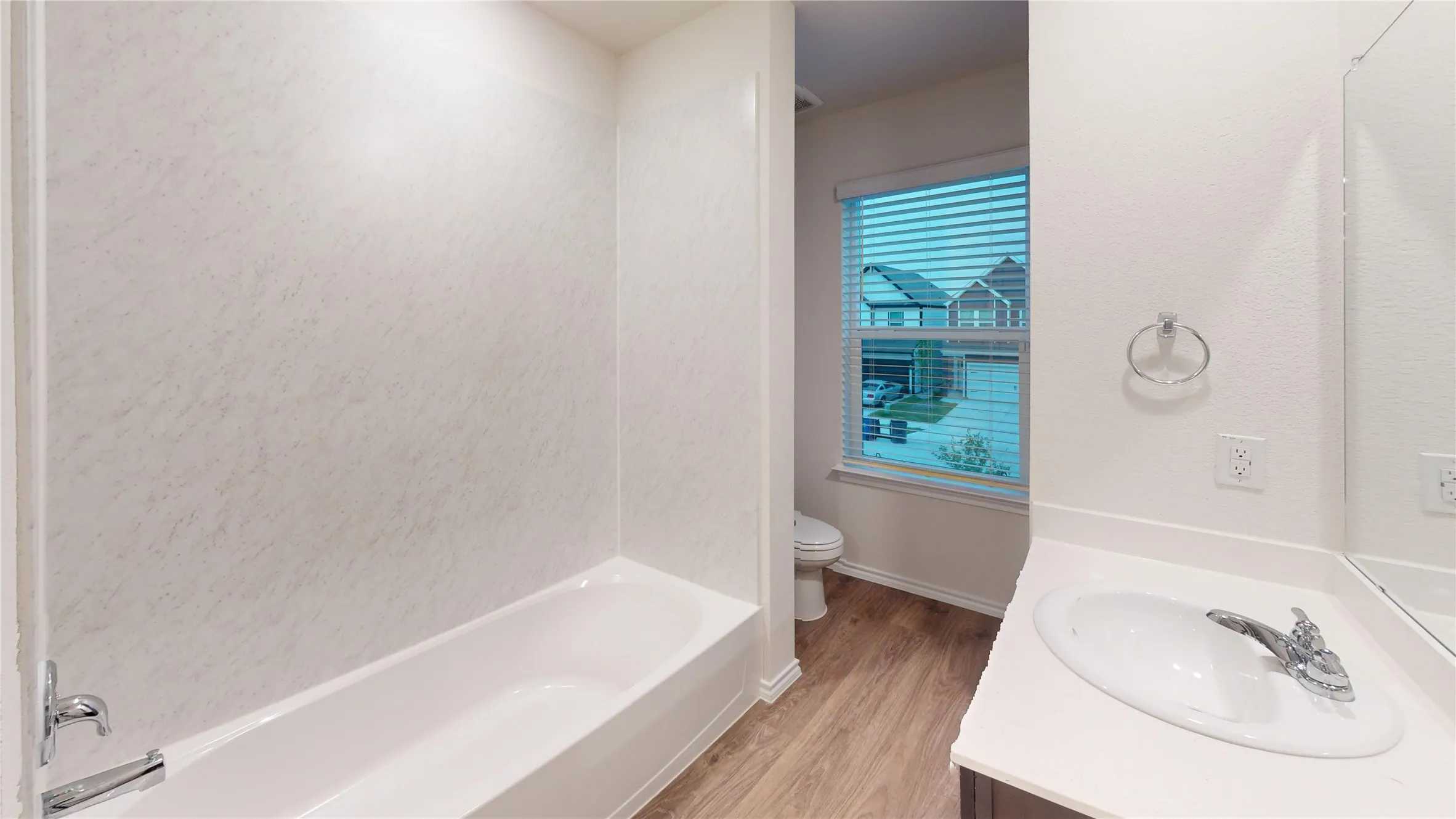 Full bathroom featuring a white tub with textured wall surround, a single vanity with an integrated sink and chrome faucet, and wood-finish flooring