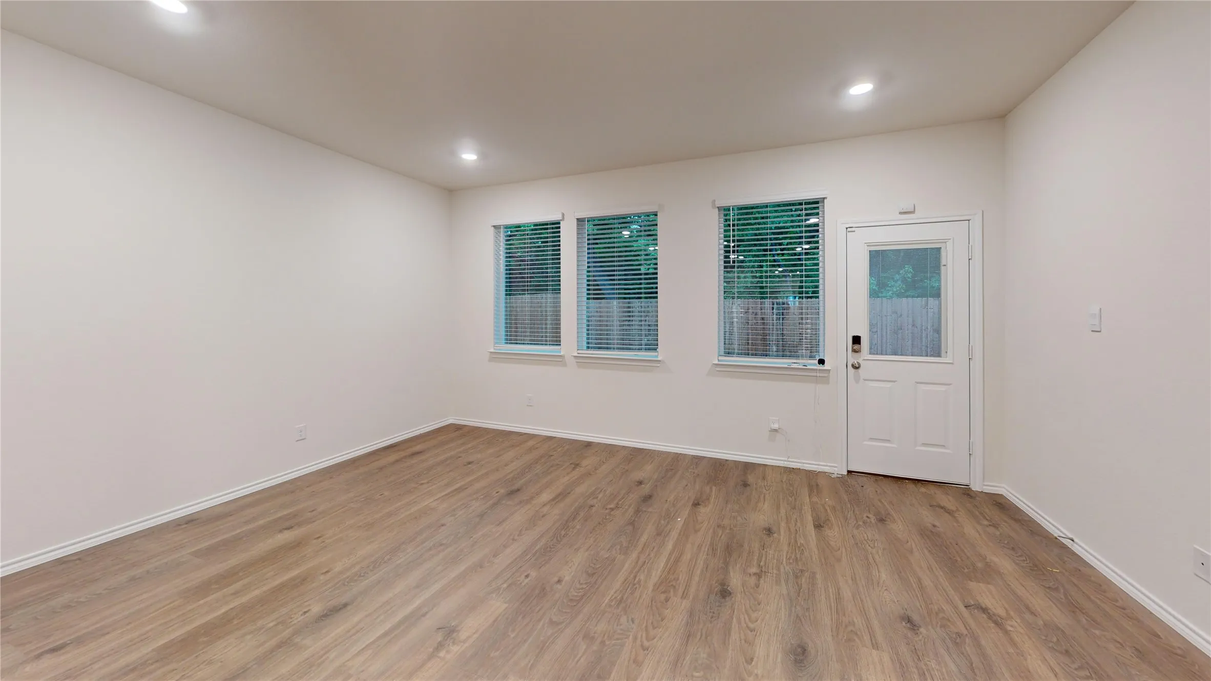Spacious room featuring wood-finish flooring, white baseboards, and recessed lighting