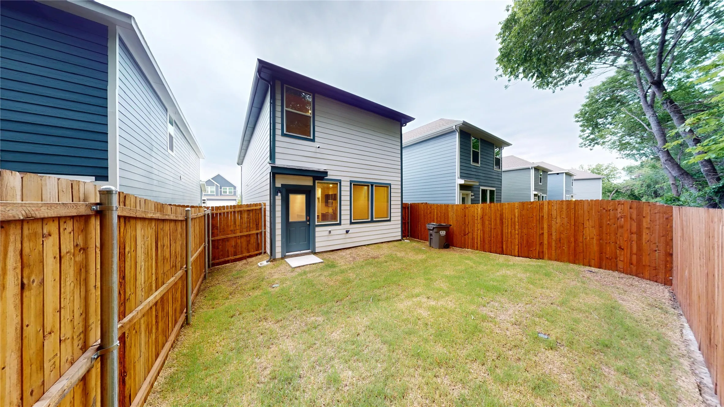 Private fenced backyard with a manicured lawn, featuring a light-colored siding exterior, multiple windows, and a rear entry door