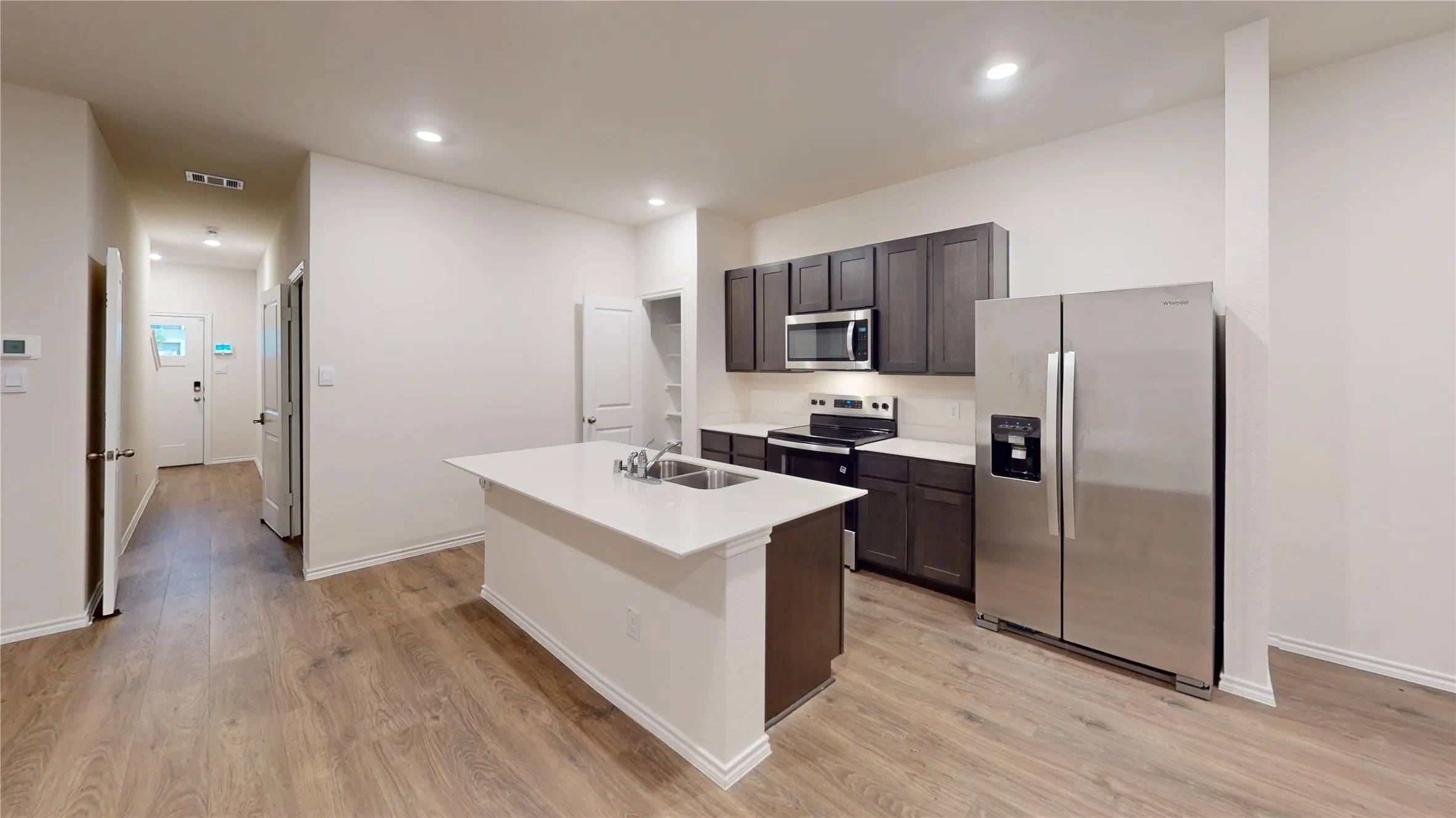 Kitchen featuring a central island with an undermount double-basin sink, quartz-finish countertops, dark wood-finish cabinetry, stainless steel appliances, and wood-finish flooring