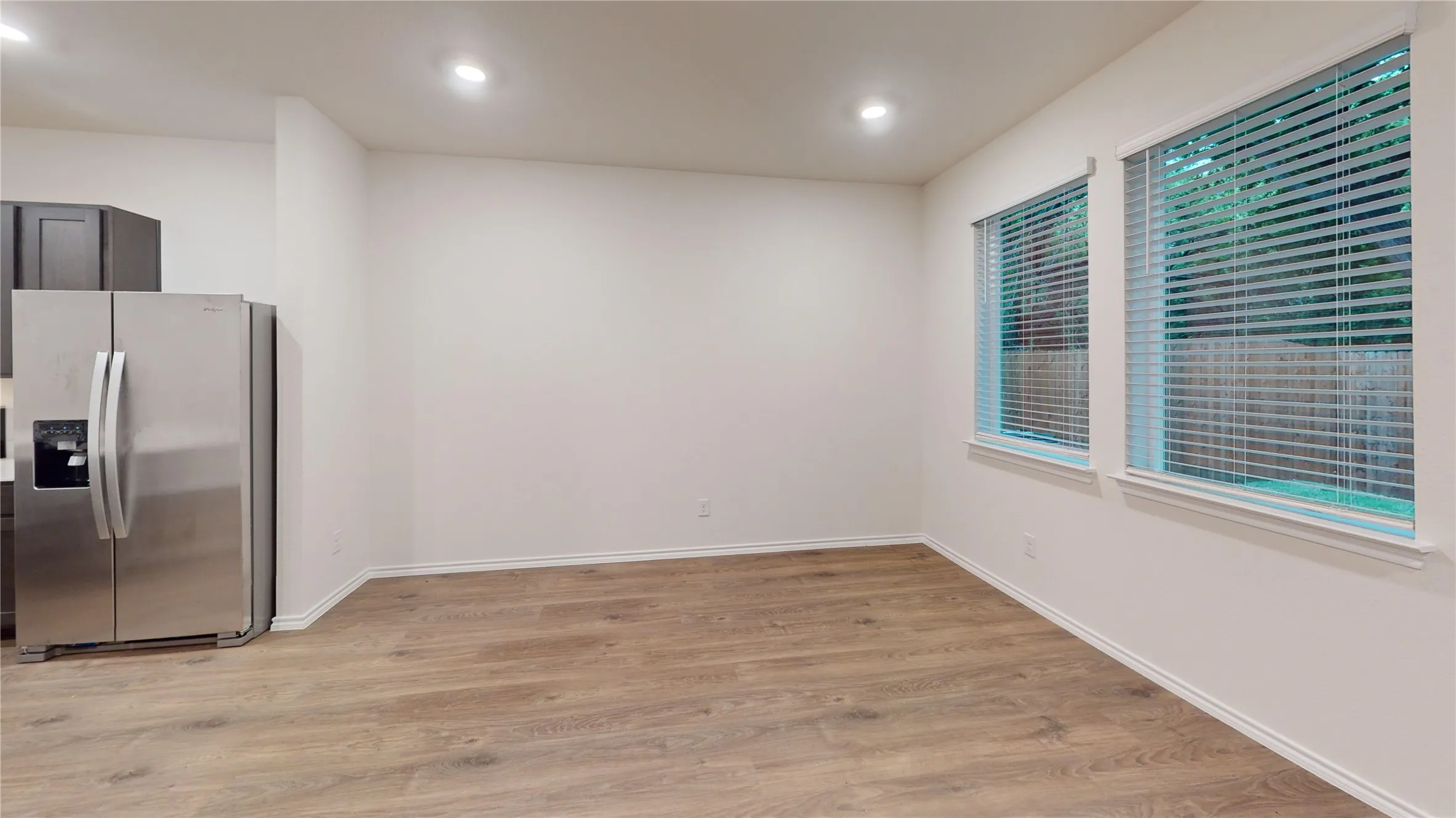 Spacious room with wood-finish flooring, recessed lighting, and two large windows featuring blinds