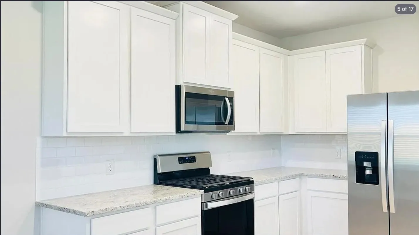 Kitchen featuring white shaker-style cabinetry, light-colored speckled countertops, a white subway tile backsplash, stainless steel appliances, and a built-in microwave