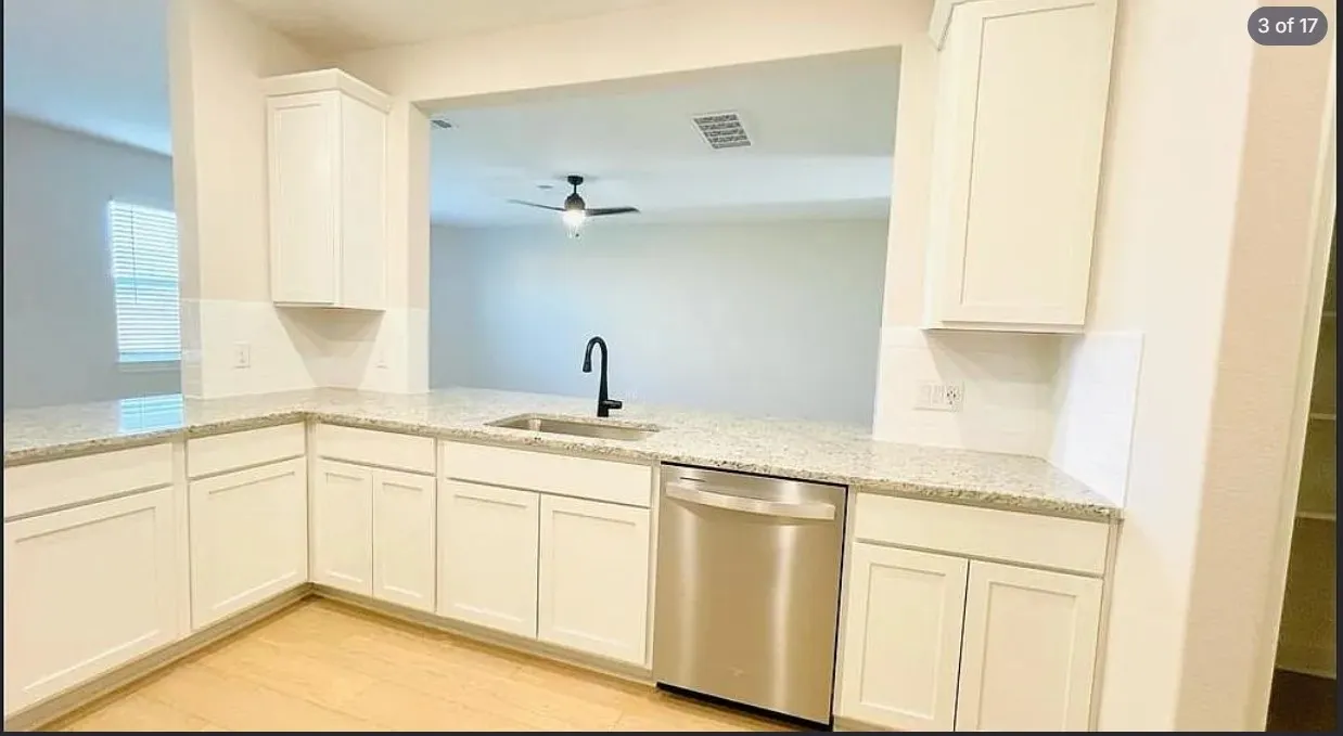 Kitchen featuring light wood-finish flooring, white cabinetry, speckled countertops, a stainless steel dishwasher, and a black gooseneck faucet