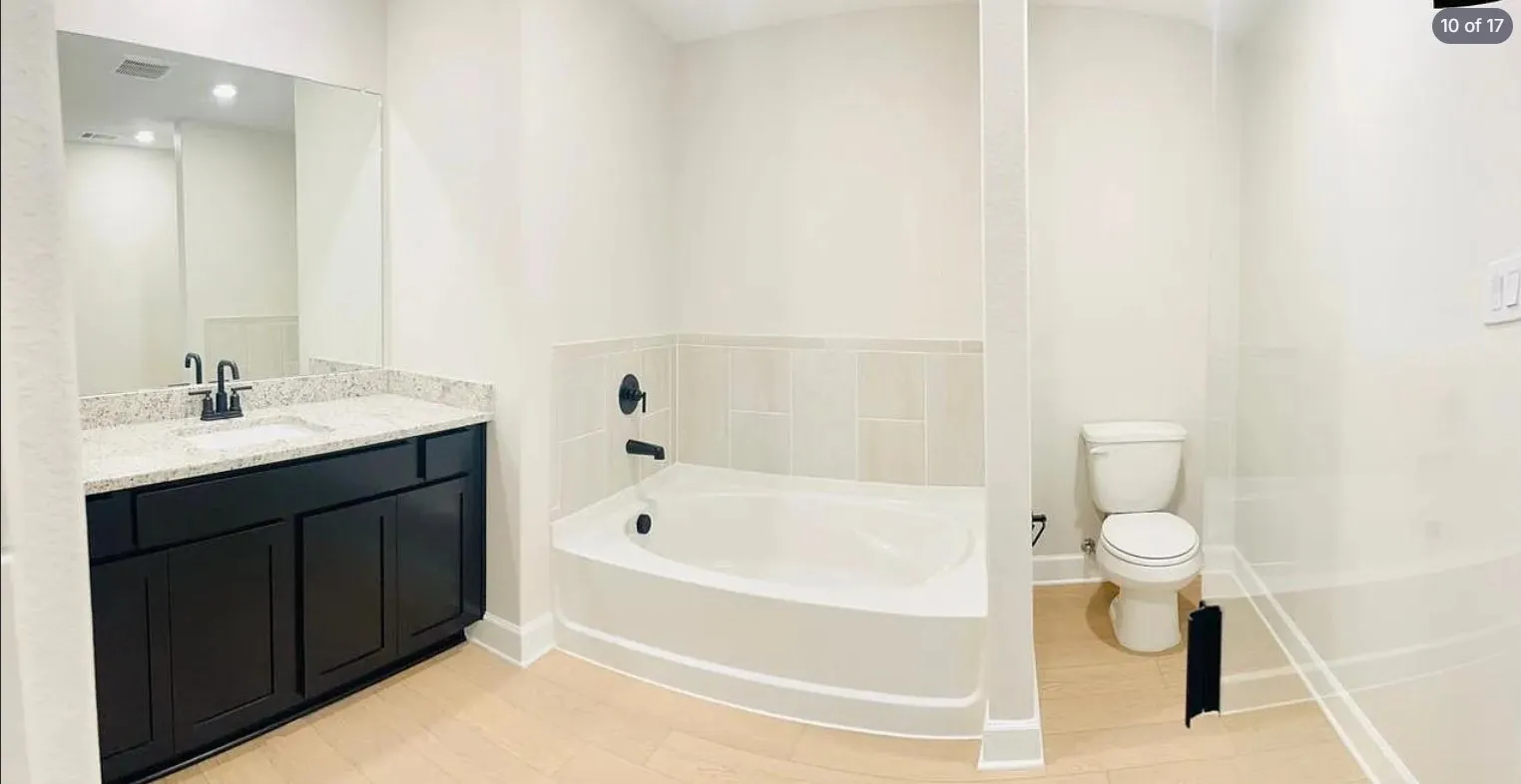 Bathroom featuring a dark wood-finish vanity with a light speckled countertop, a white soaking tub with black fixtures, and light wood-finish flooring