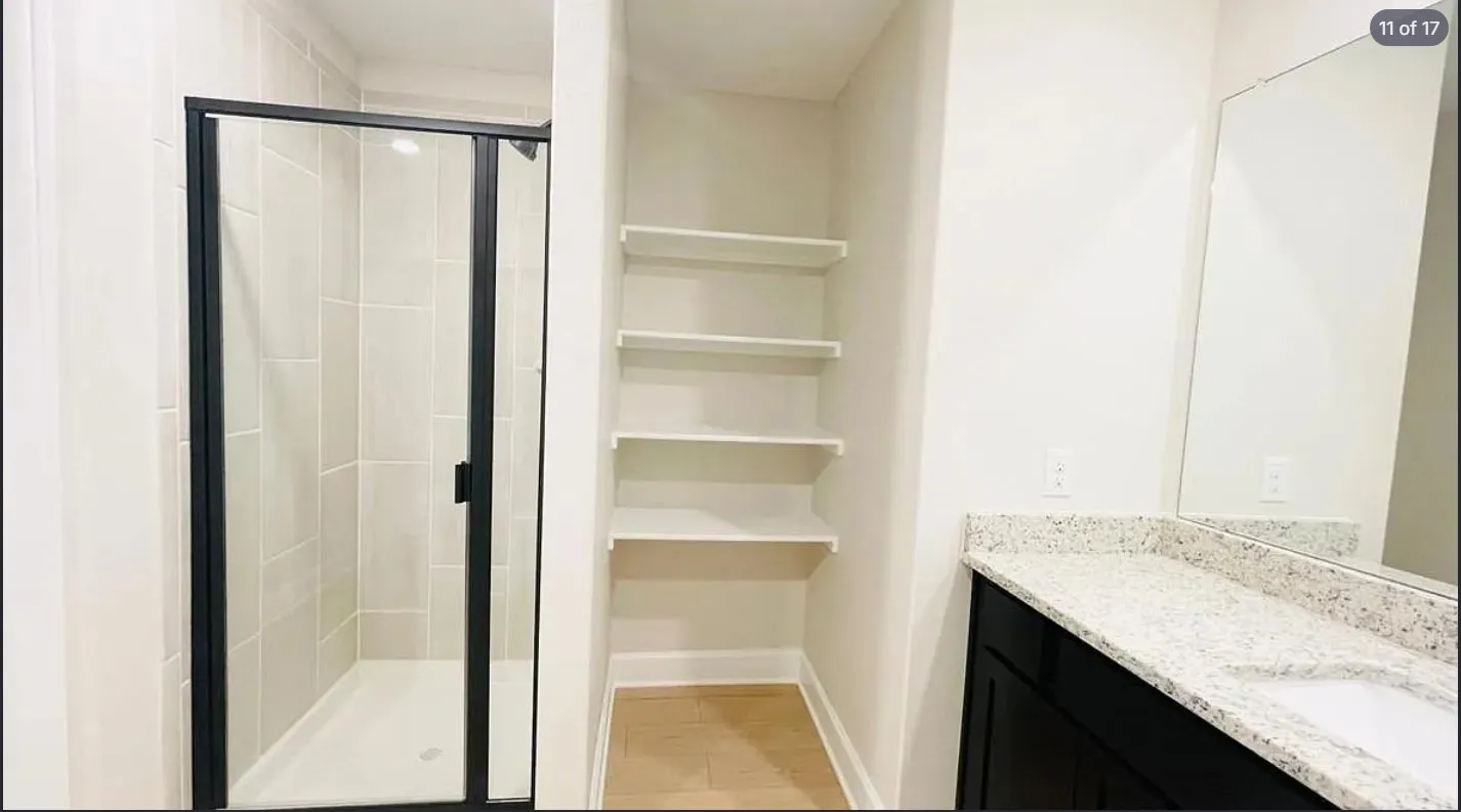 Bathroom featuring a glass-enclosed shower with tiled walls, built-in shelving, and a vanity with a light-toned countertop and dark cabinetry
