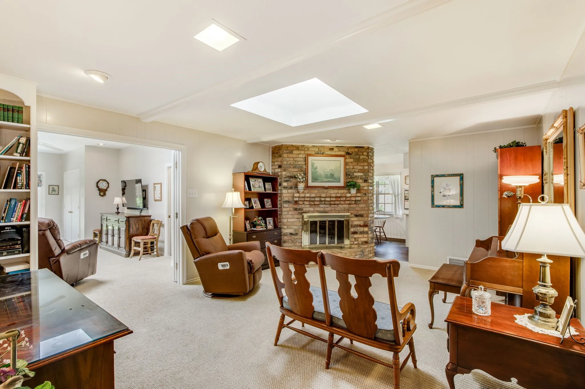 Carpeted living space featuring a brick fireplace with a metal grate, built-in shelving, and a prominent skylight