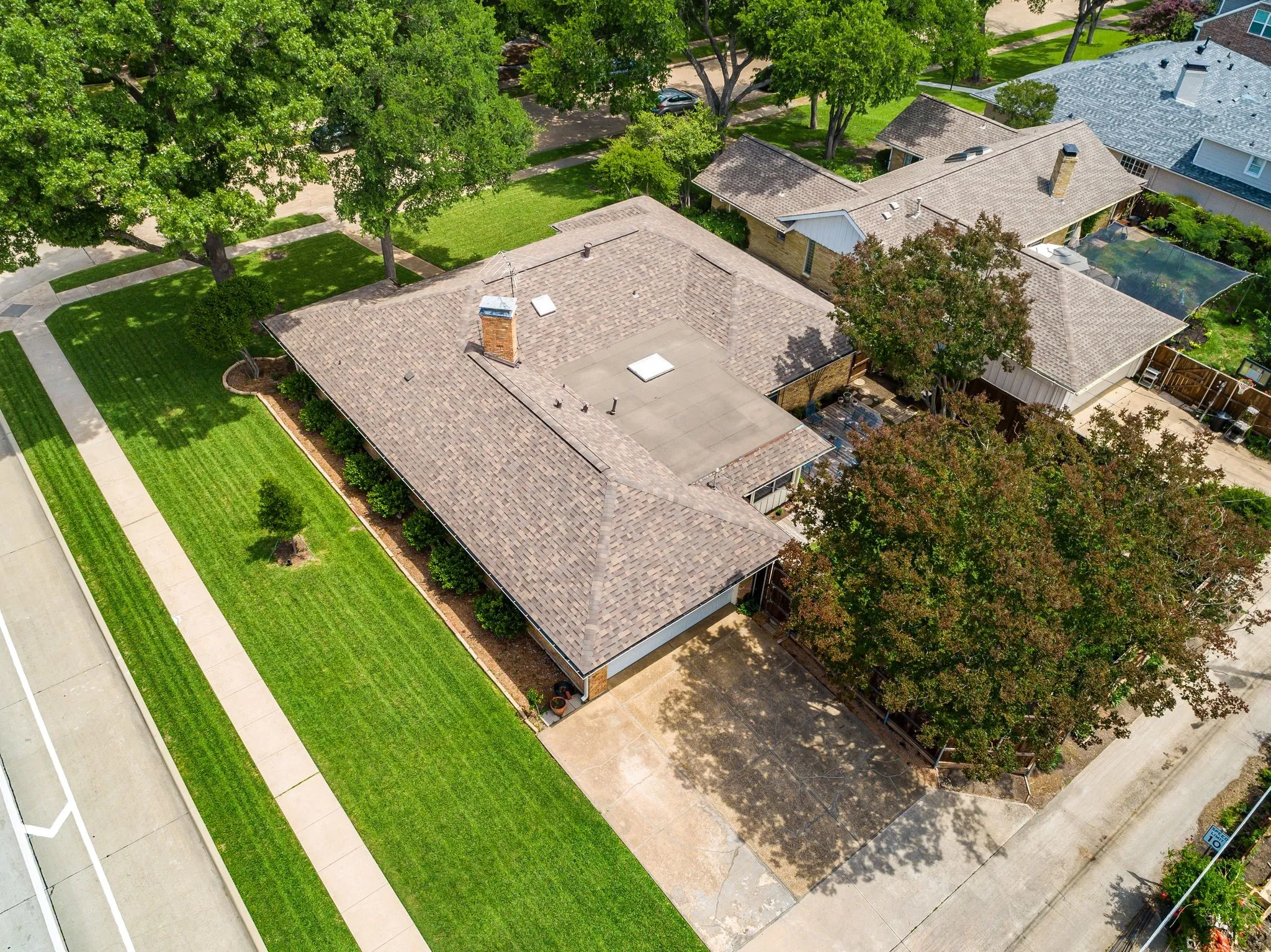 Expansive property featuring a brown shingle roof, a brick chimney, a dedicated driveway, and mature landscaping with established trees and manicured lawns