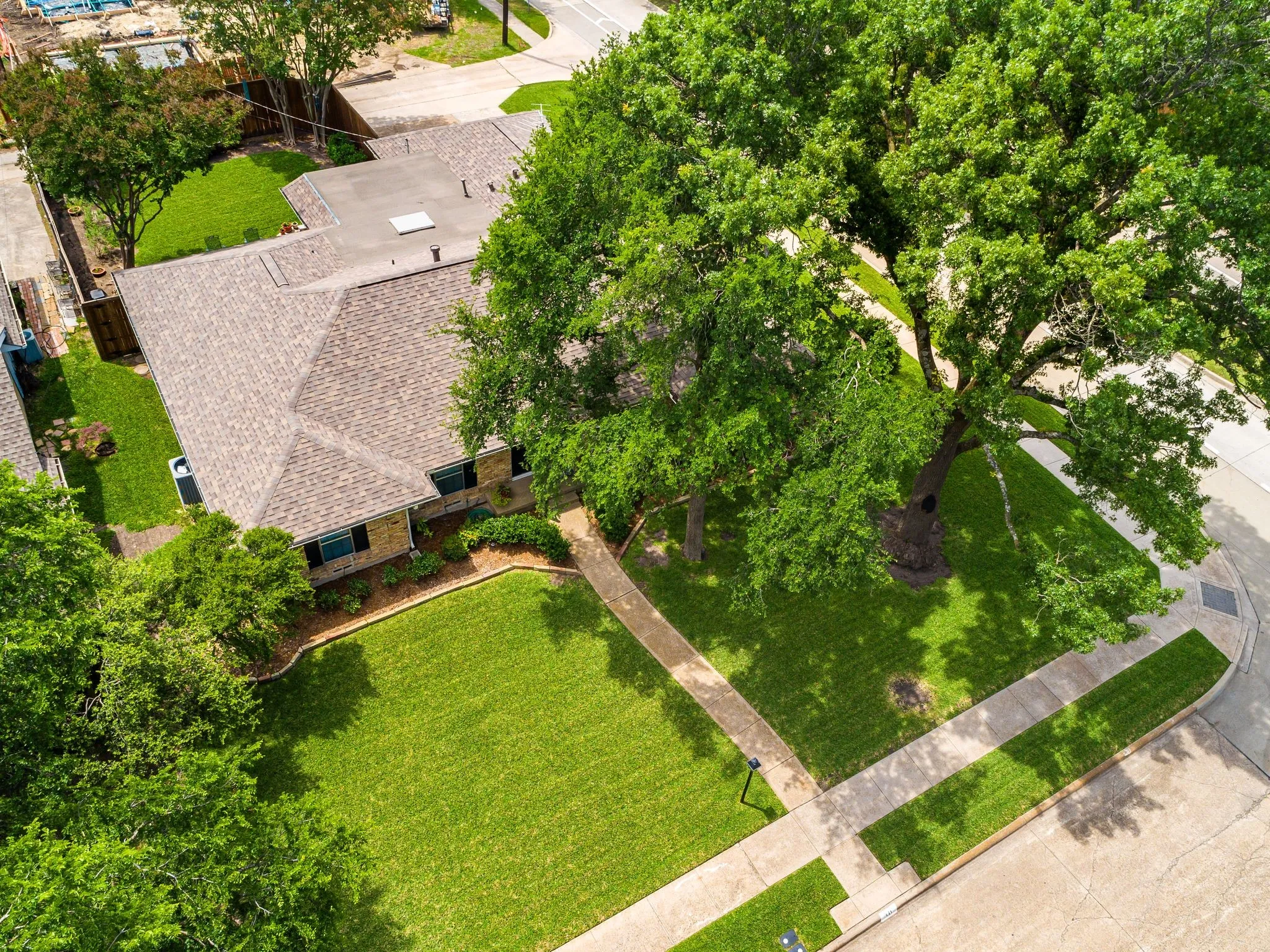Aerial perspective showcasing a single-story residence with a pitched shingle roof, a manicured front lawn, and established perimeter landscaping
