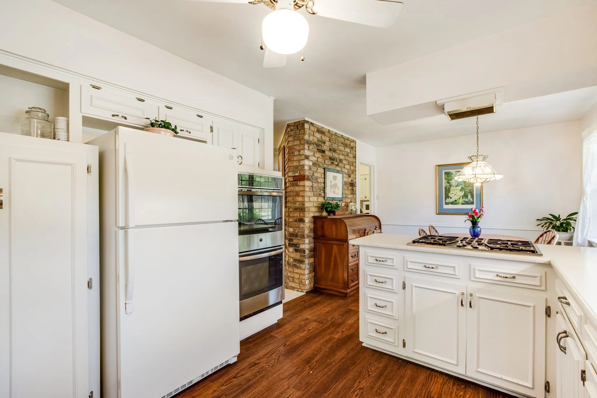 Kitchen featuring wood-finish flooring, white cabinetry, integrated double oven, and a cooktop on the center island
