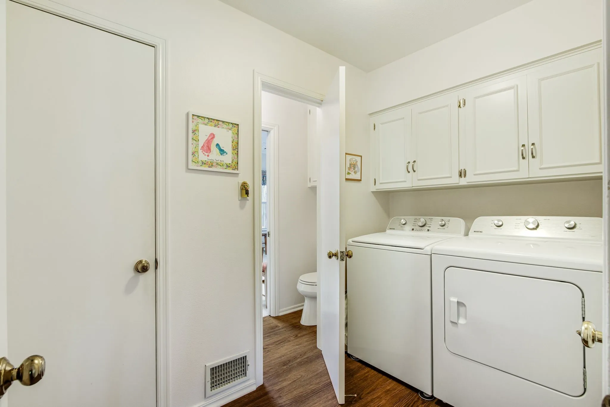 Laundry area featuring wood-finish flooring, white cabinetry, and a utility closet