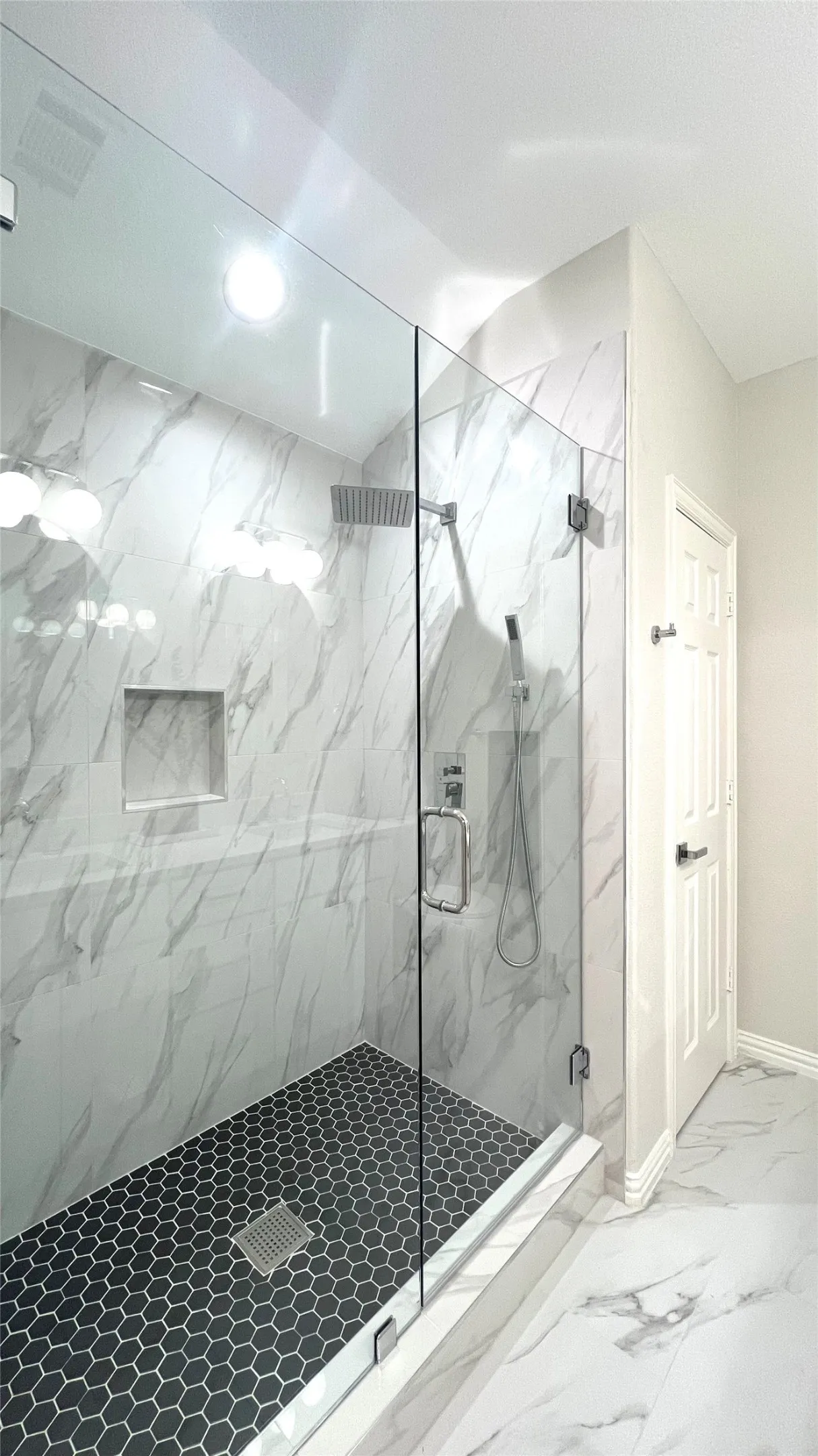Walk-in shower with clear glass enclosure and black hexagonal tile flooring