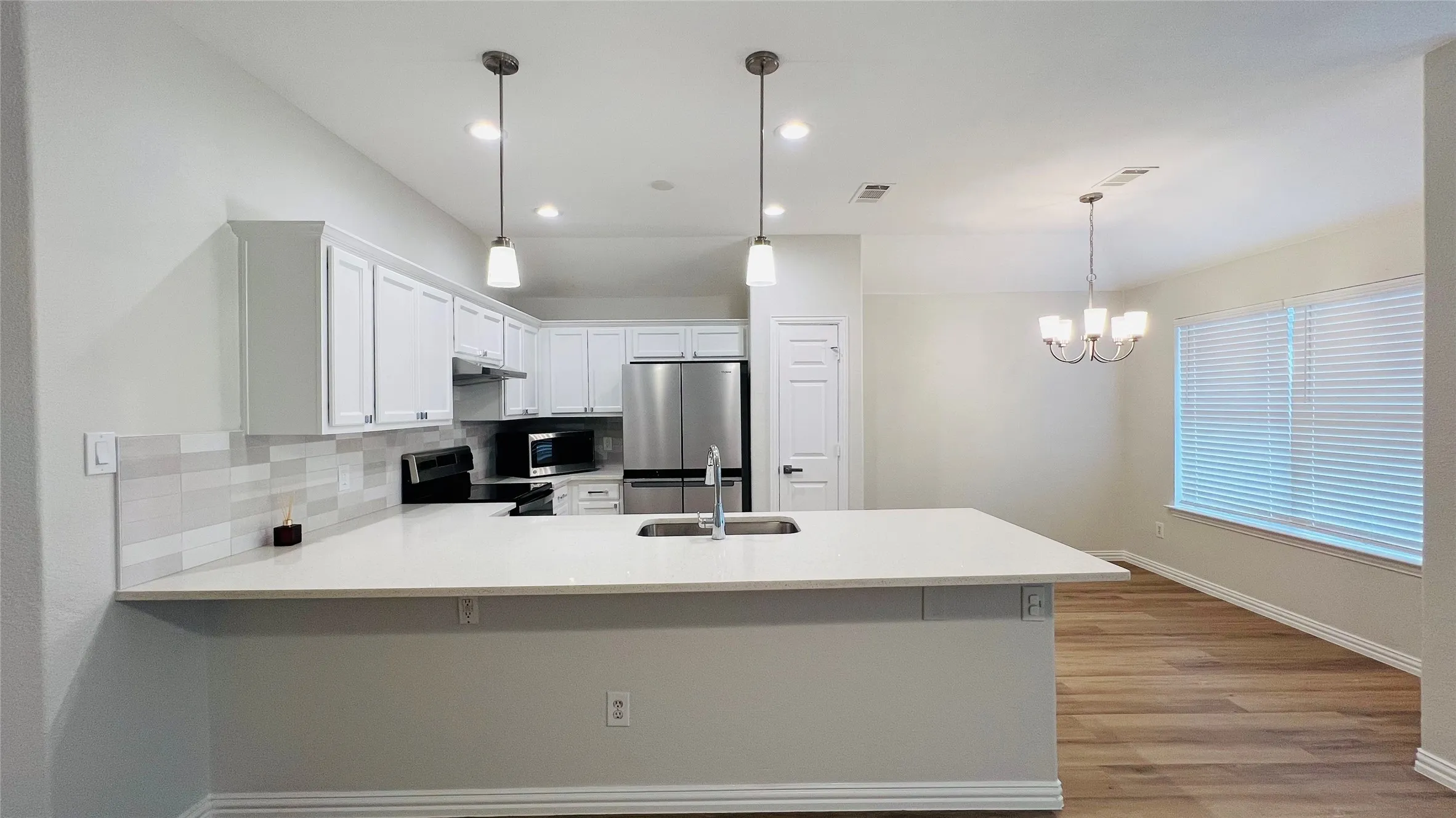 Contemporary kitchen featuring a large island with an undermount sink, white cabinetry, stainless steel appliances, and a tiled backsplash