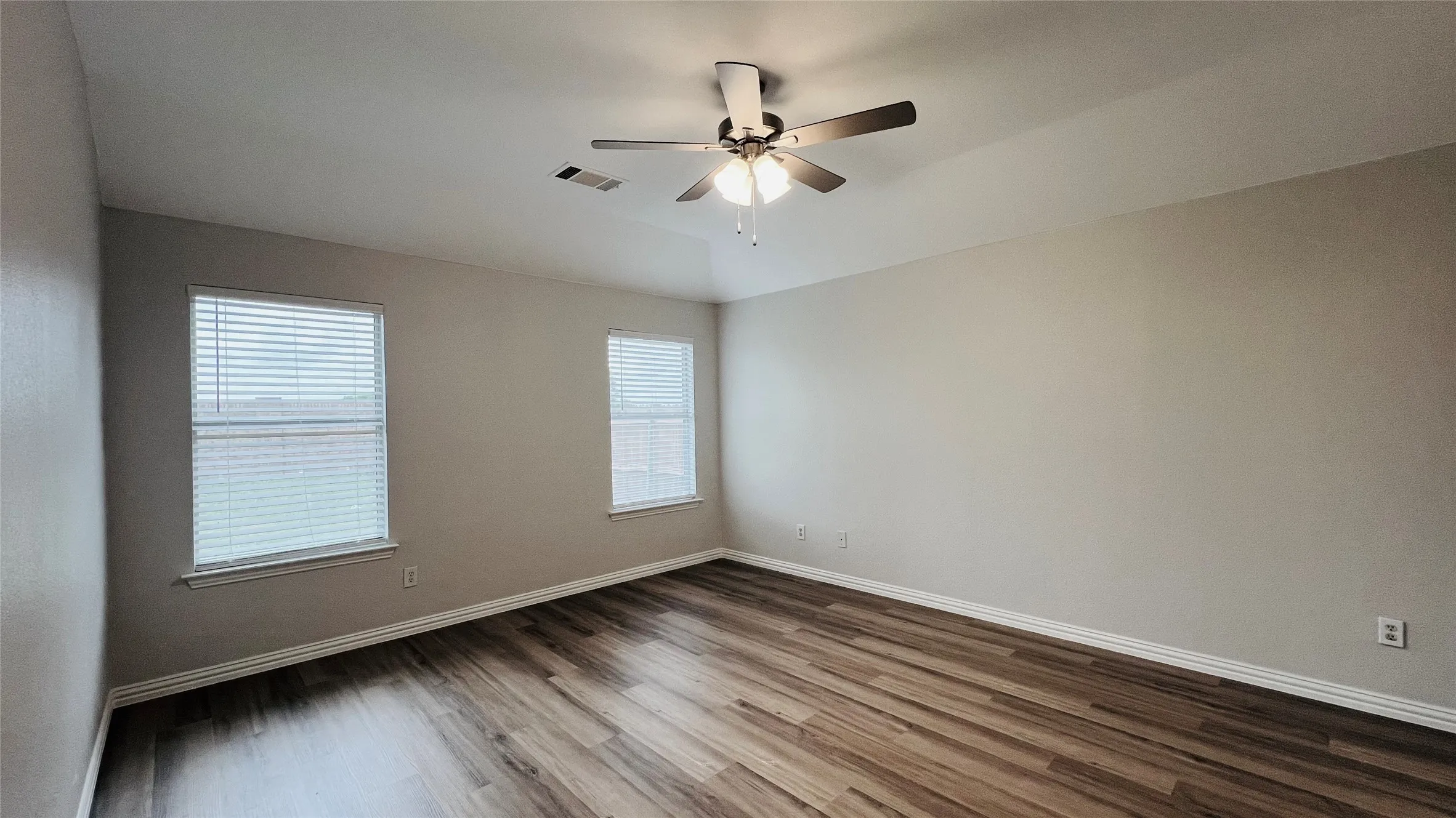 Spacious room featuring wood-finish flooring, neutral-toned walls, and a ceiling fan with integrated lighting