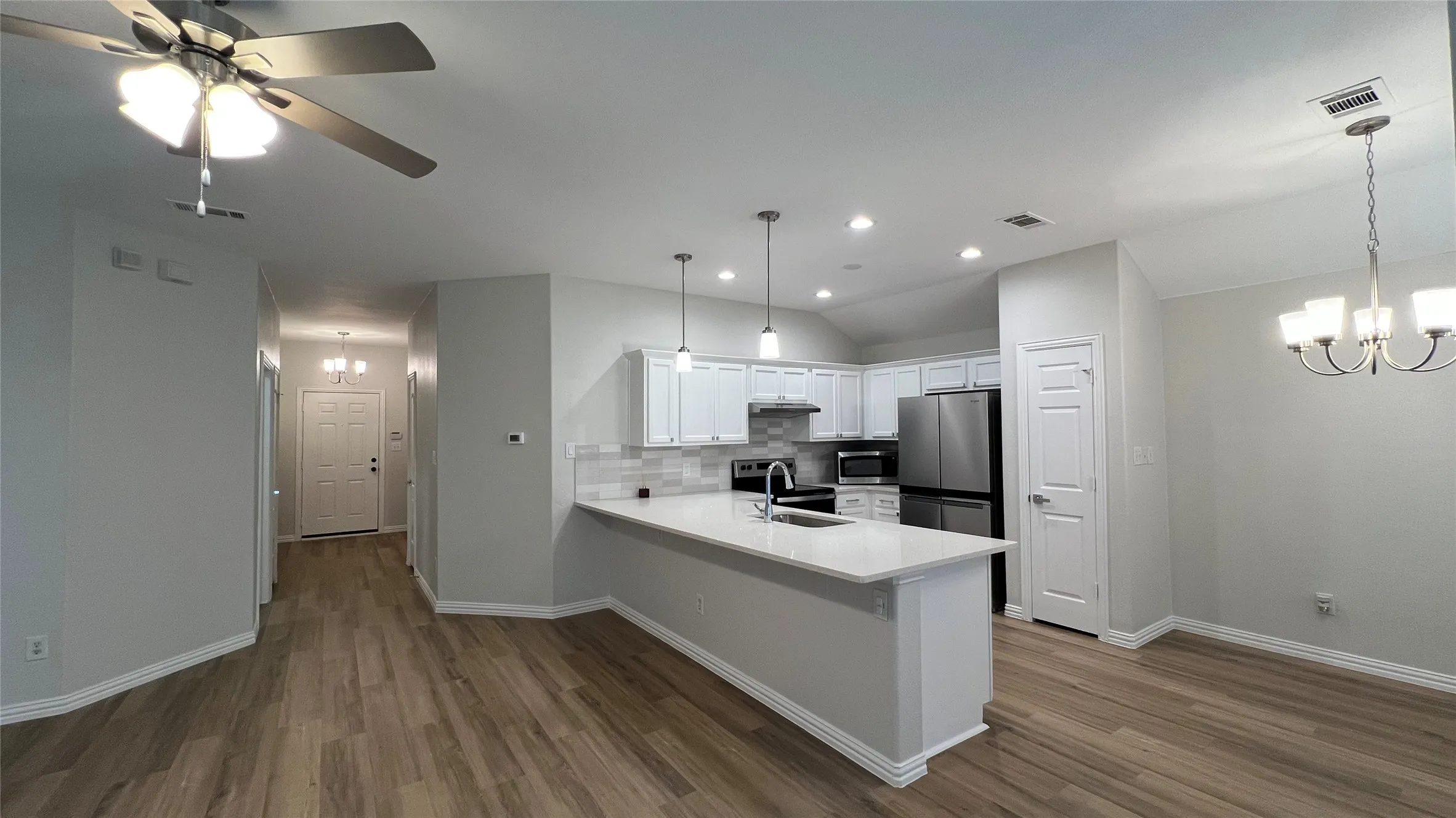 Open-concept kitchen and dining area featuring wood-finish flooring, white cabinetry, a kitchen island with pendant lighting, stainless steel appliances, and a tiled backsplash