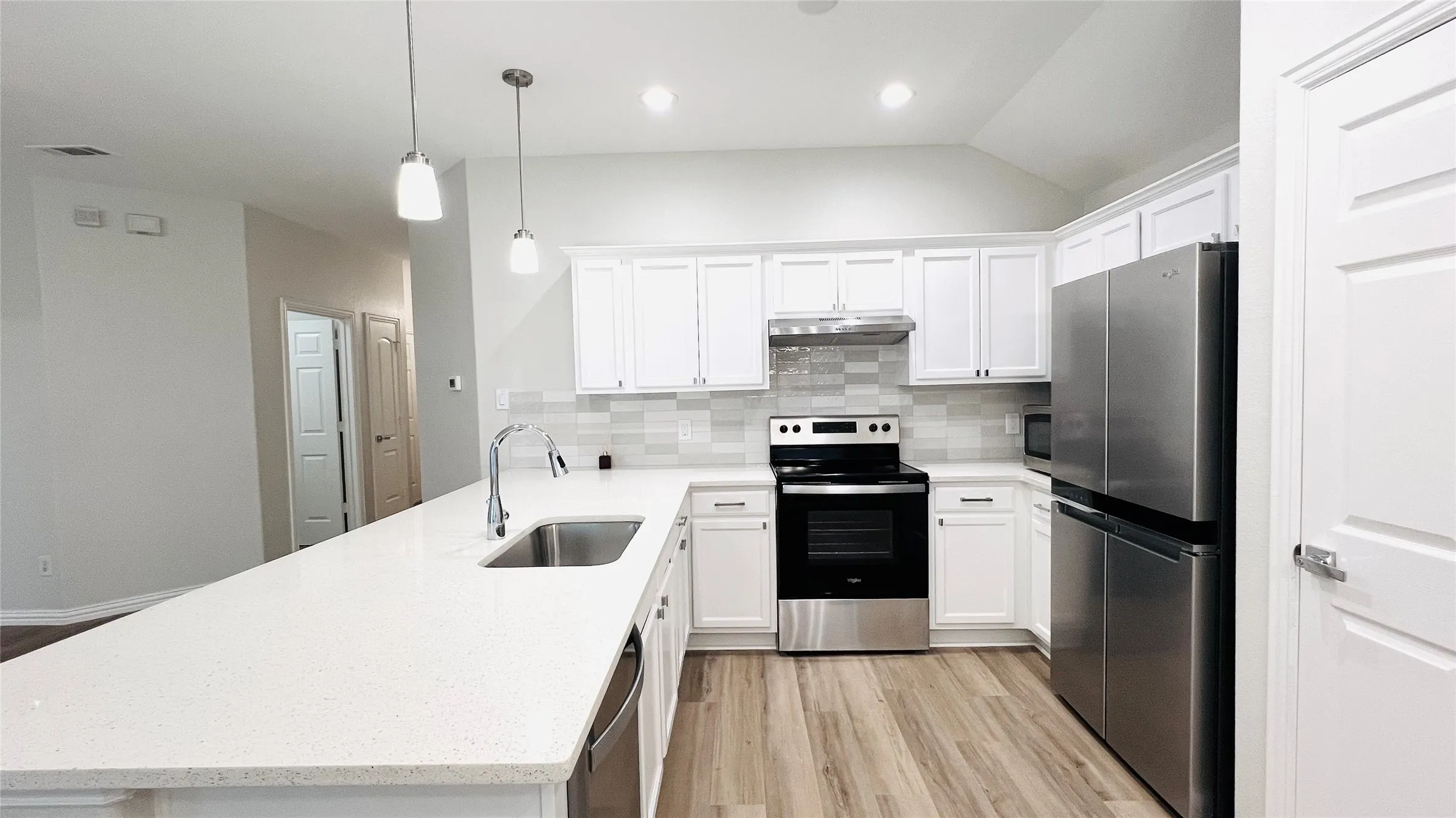 Modern kitchen featuring a large white countertop, stainless steel appliances, white cabinetry, and wood-finish flooring