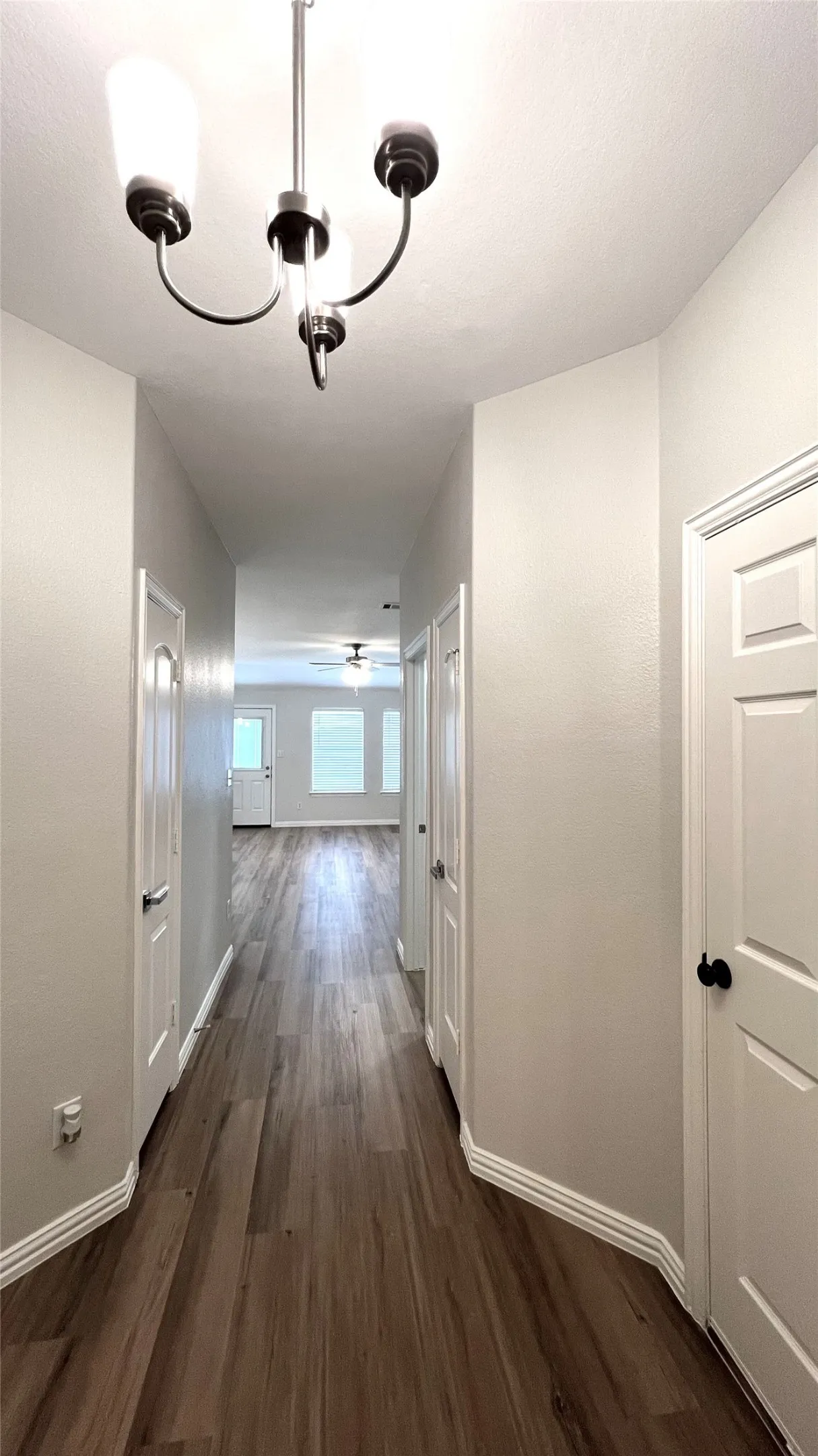 Long hallway featuring wood-finish flooring, white baseboards, and light gray walls