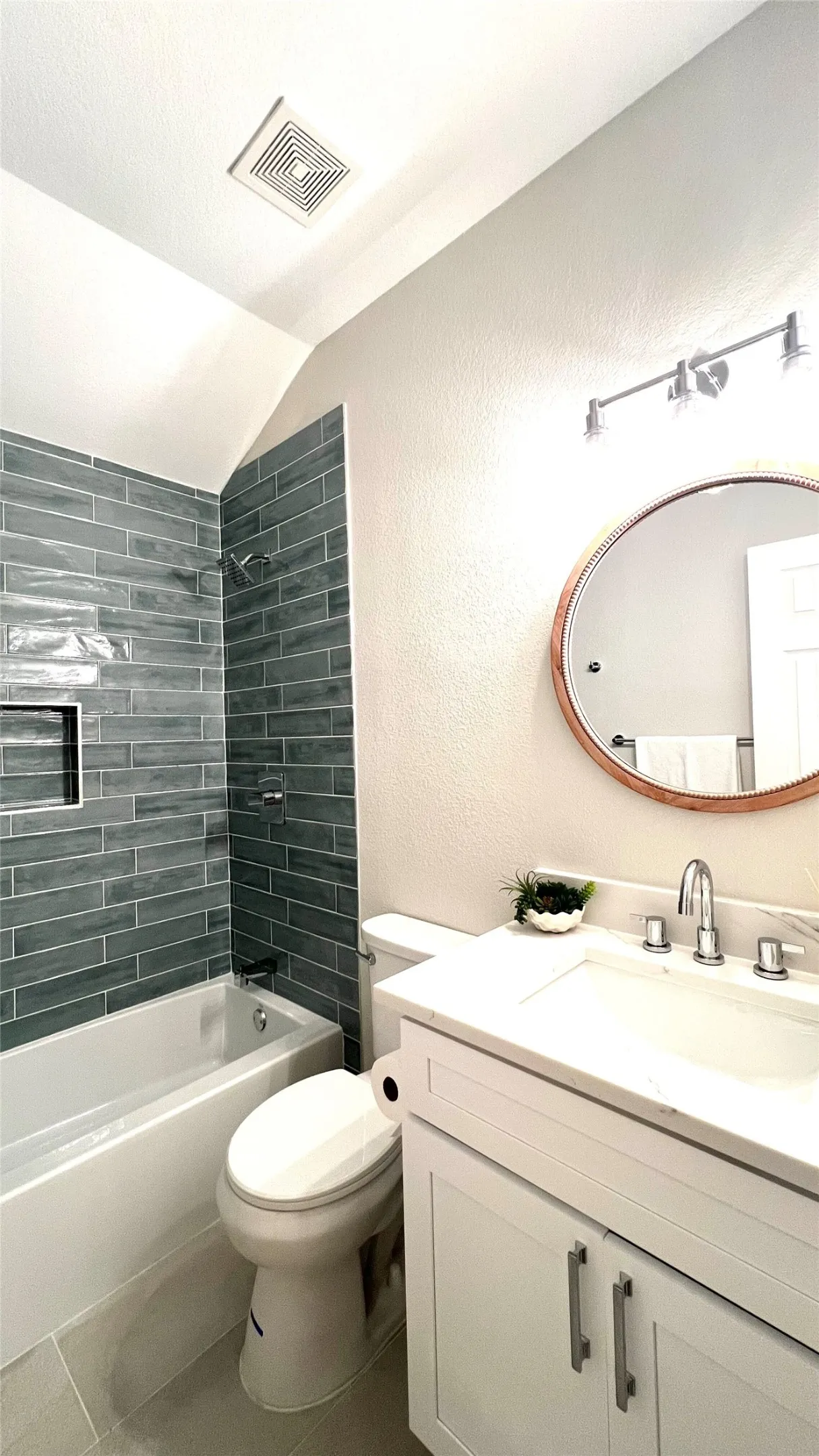 Bathroom featuring a white vanity with a rectangular sink, a round frameless mirror, and a tiled shower-bathtub combination with an integrated niche