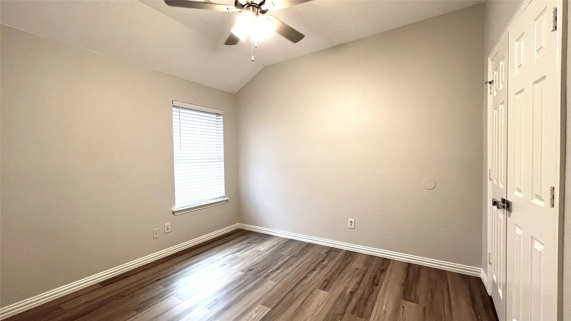 Room featuring vaulted ceilings, wood-finish flooring, a ceiling fan with light fixture, window with blinds, and white bi-fold closet doors