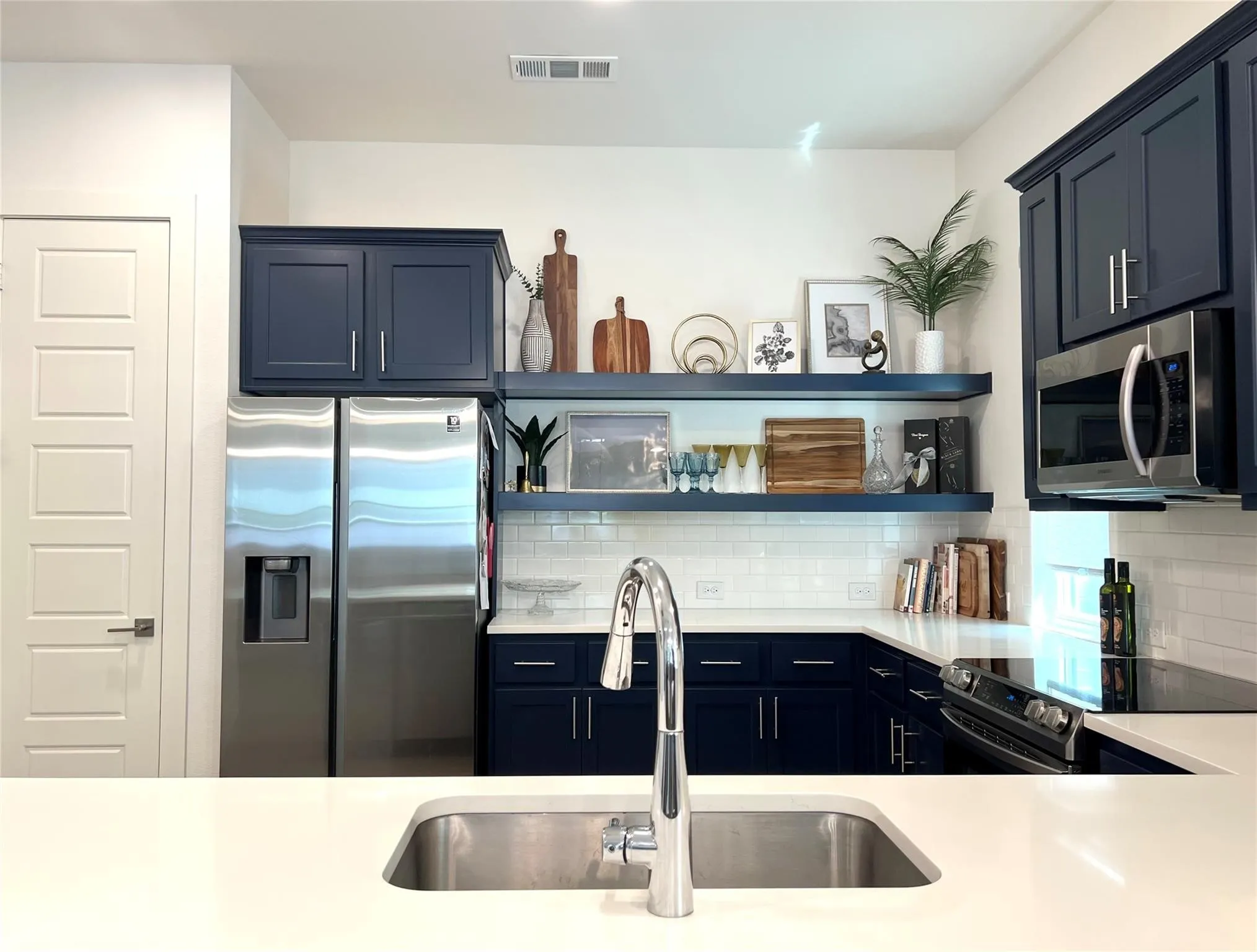 Kitchen with tasteful backsplash, appliances with stainless steel finishes, blue cabinets, and floating shelves