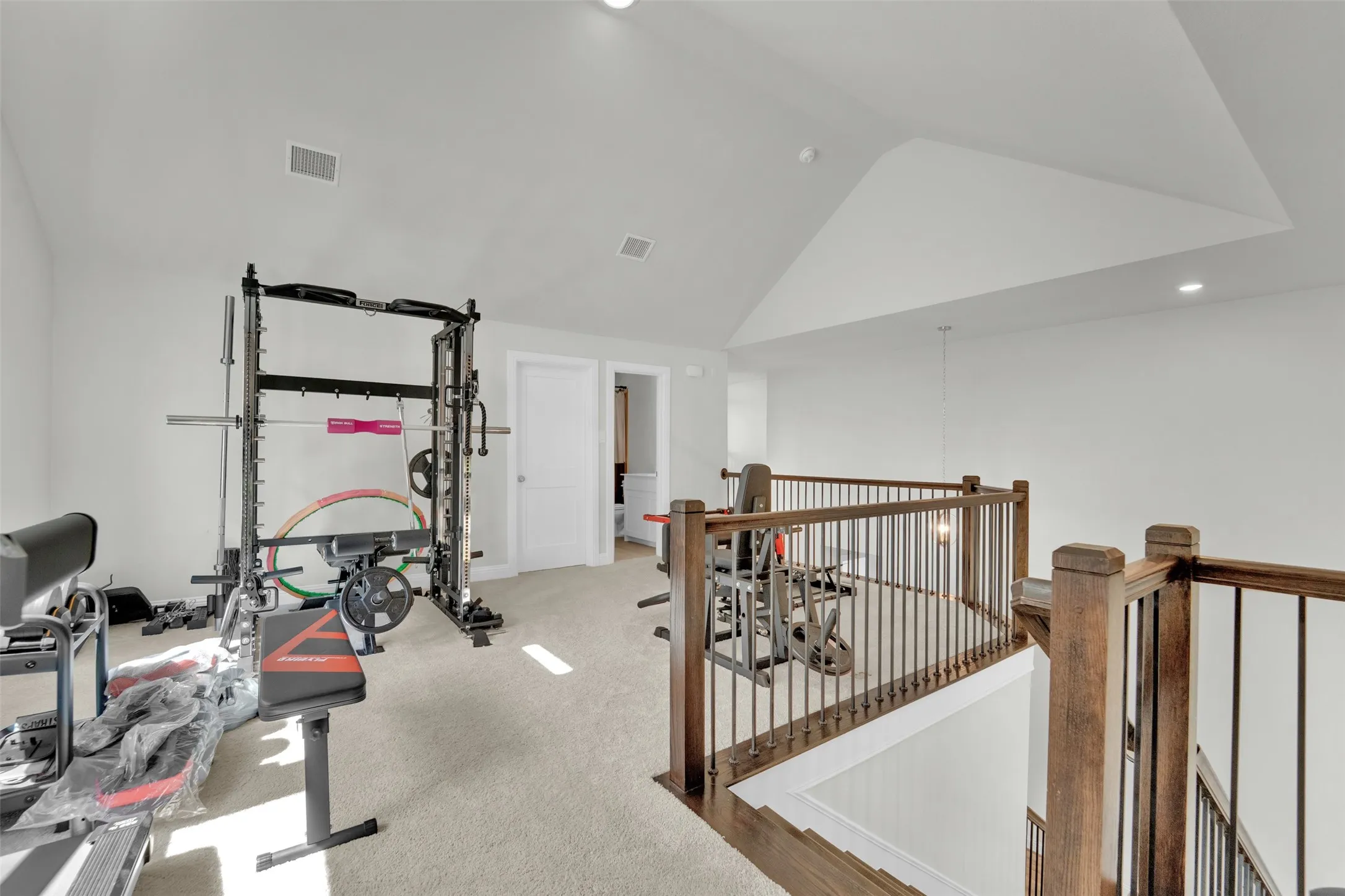 Carpeted loft area featuring a vaulted ceiling, recessed lighting, and a dark wood and metal spindle railing overlooking a lower level