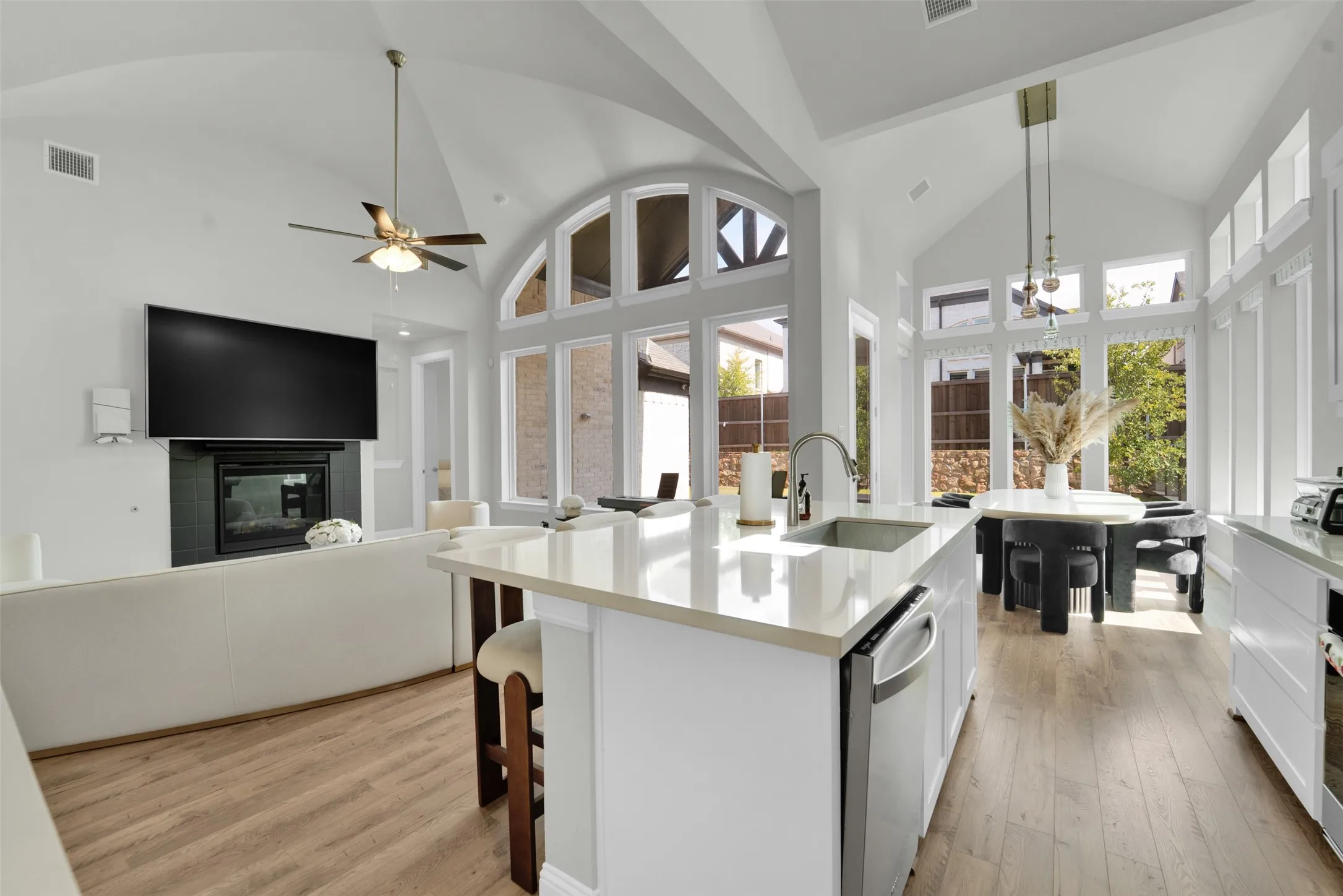 Open-concept living space with vaulted ceilings, expansive windows, a central island with countertop seating, wood-finish flooring, and a built-in fireplace