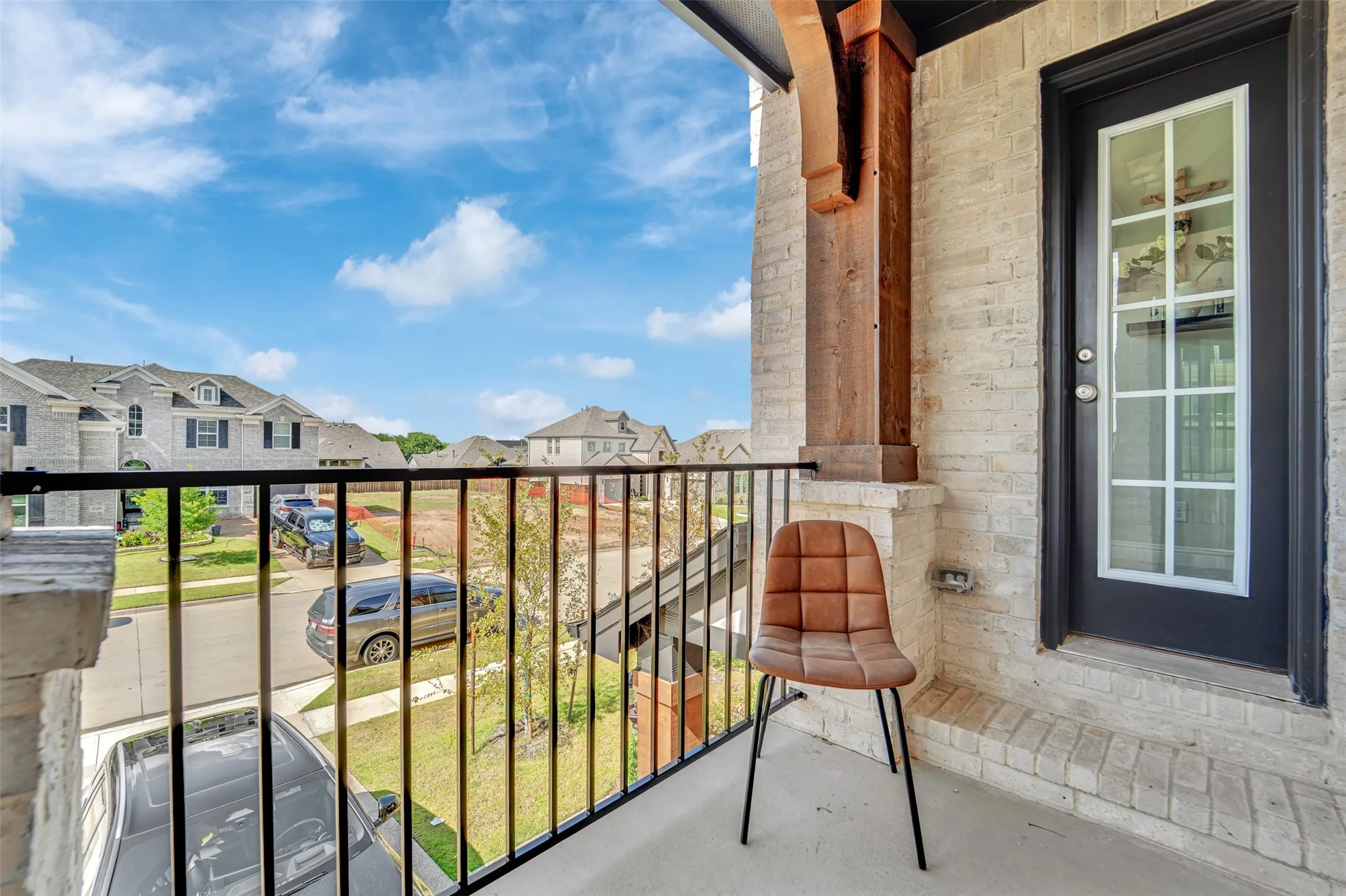 Balcony featuring light-colored brick, a black iron railing, a dark entry door with glass panels, a concrete floor, and an exposed wood beam detail